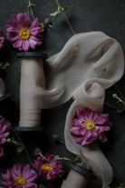 A mauve ribbon on black wooden spool draped on a dark surface, with scattered mauve flowers with yellow centers.
