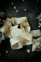 Dark textured background with eco-print silk ribbons and scattered petals on a dark background