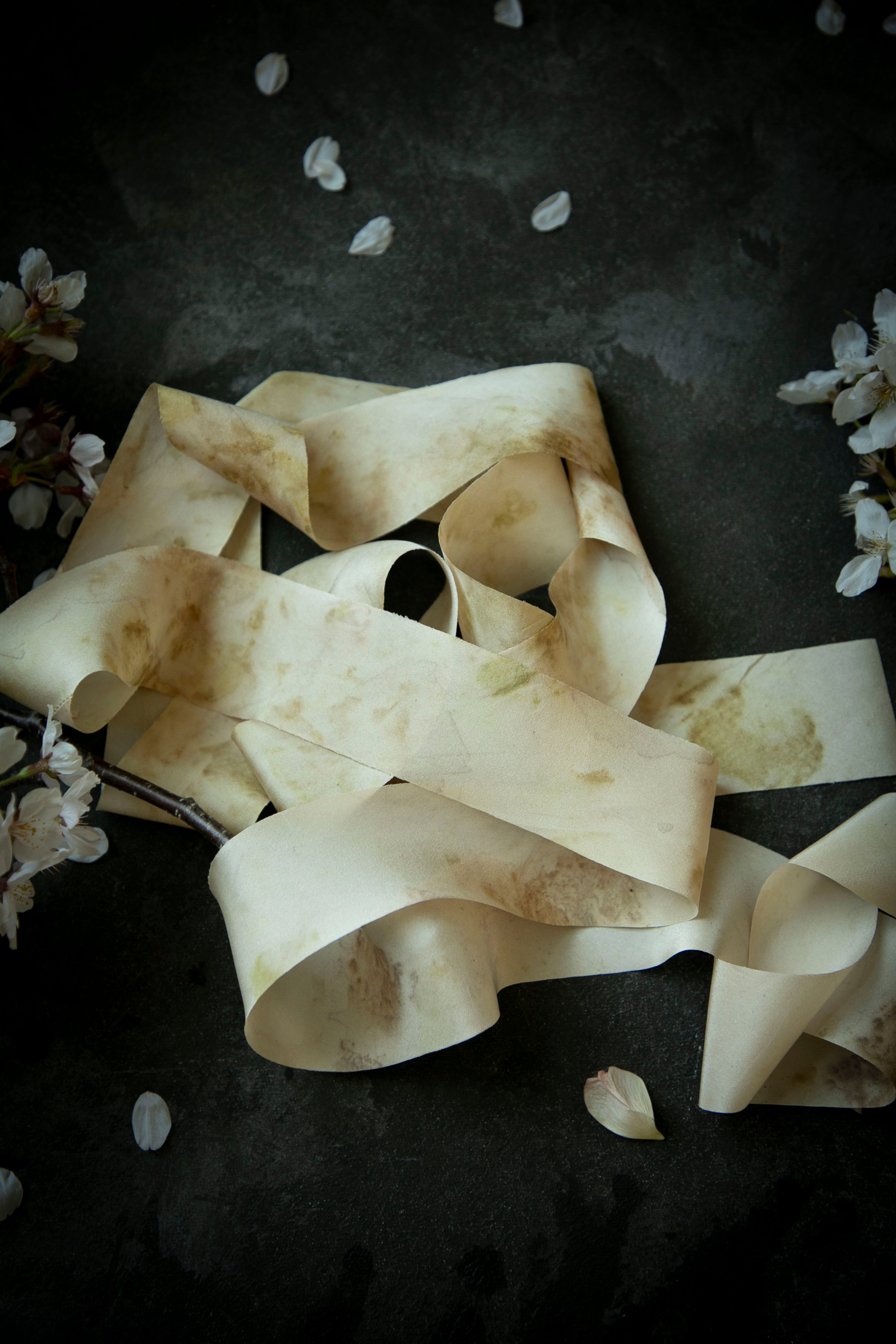 Dark textured background with eco-print silk ribbons and scattered petals on a dark background