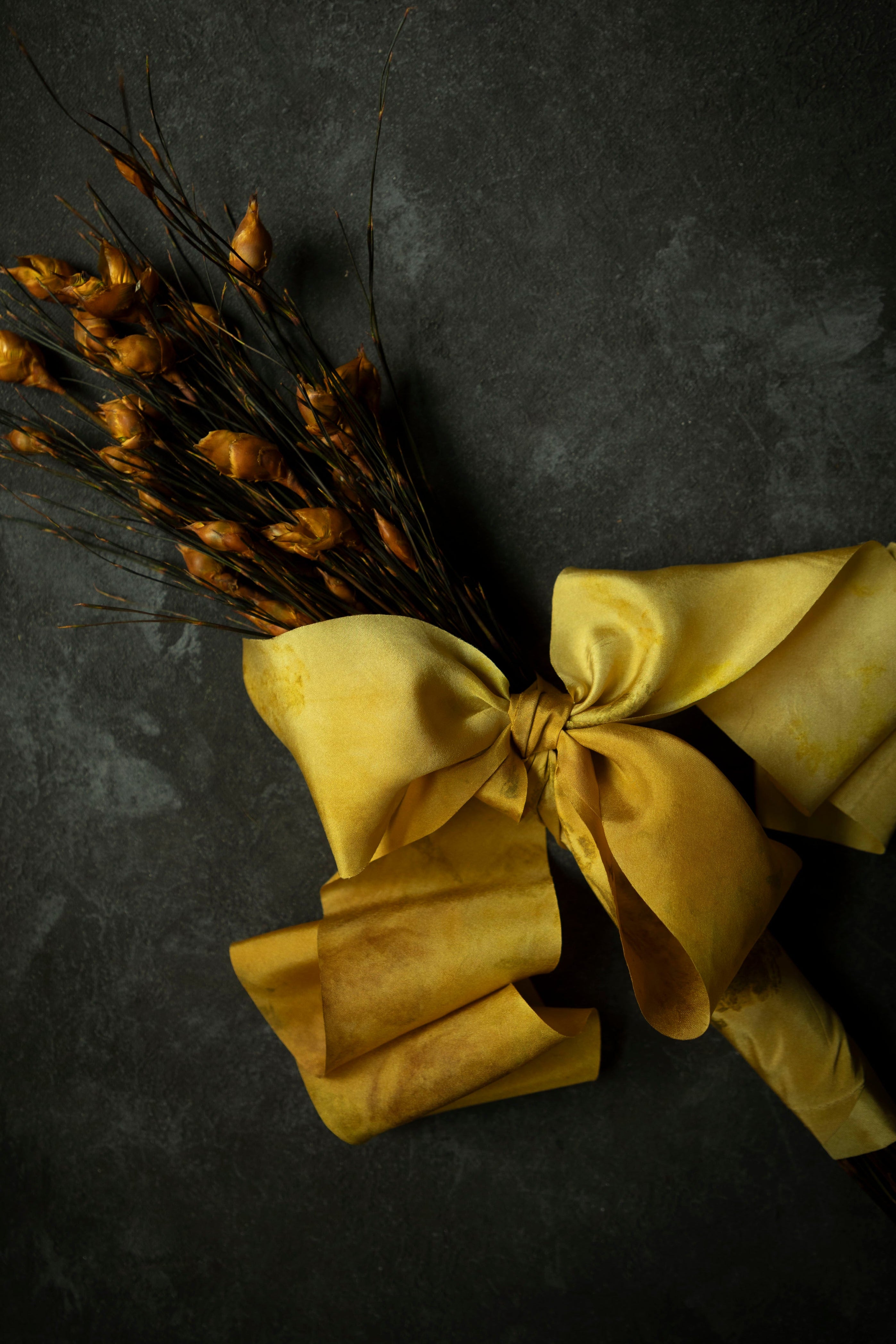 Bouquet of dried yellow flowers with a large yellow bow on a dark background