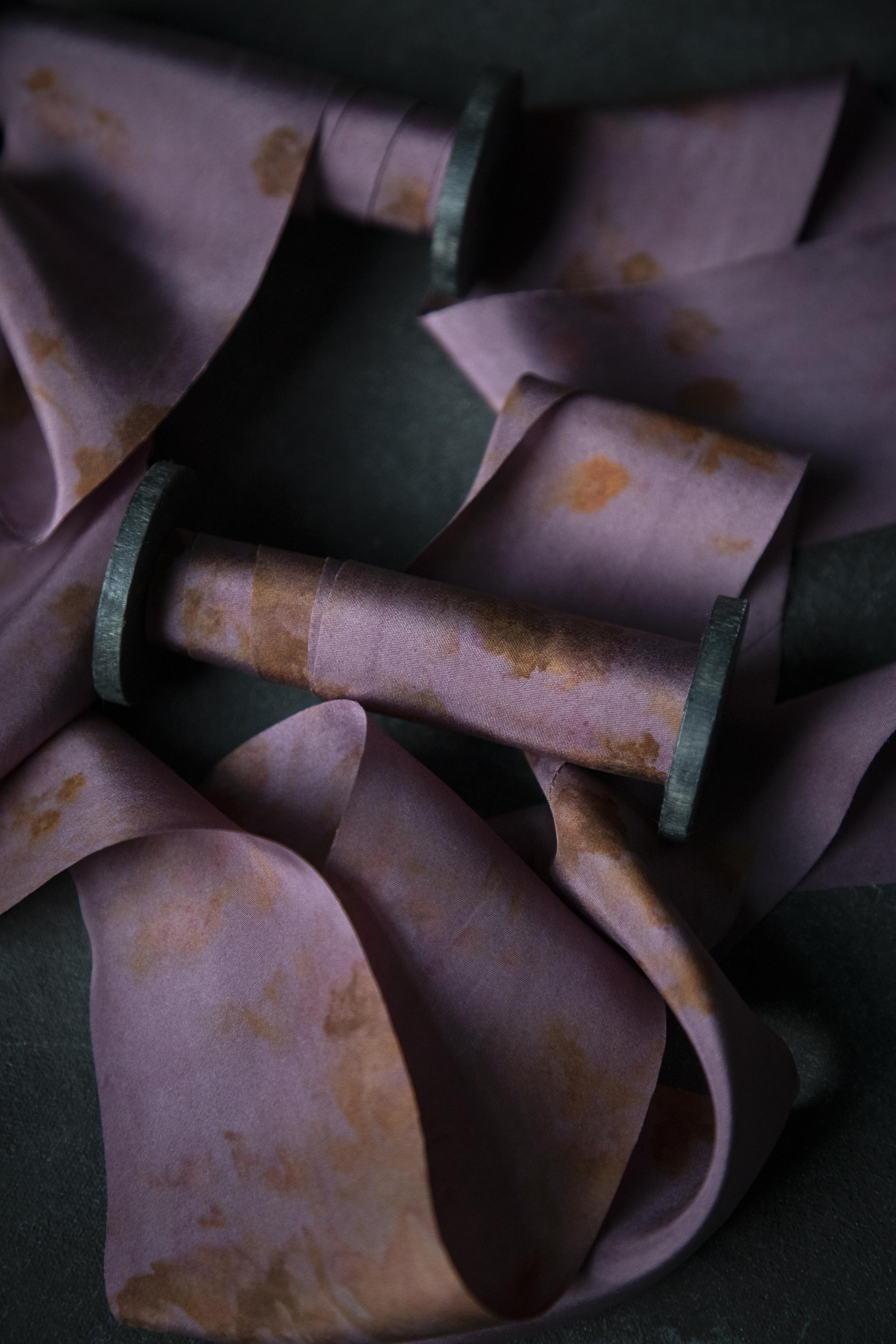 Close-up of a purple fabric with rust-colored stains on a dark background