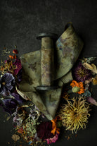 Limited-edition eco-print silk ribbon displayed on a wood spool surrounded by an assortment of dried flowers