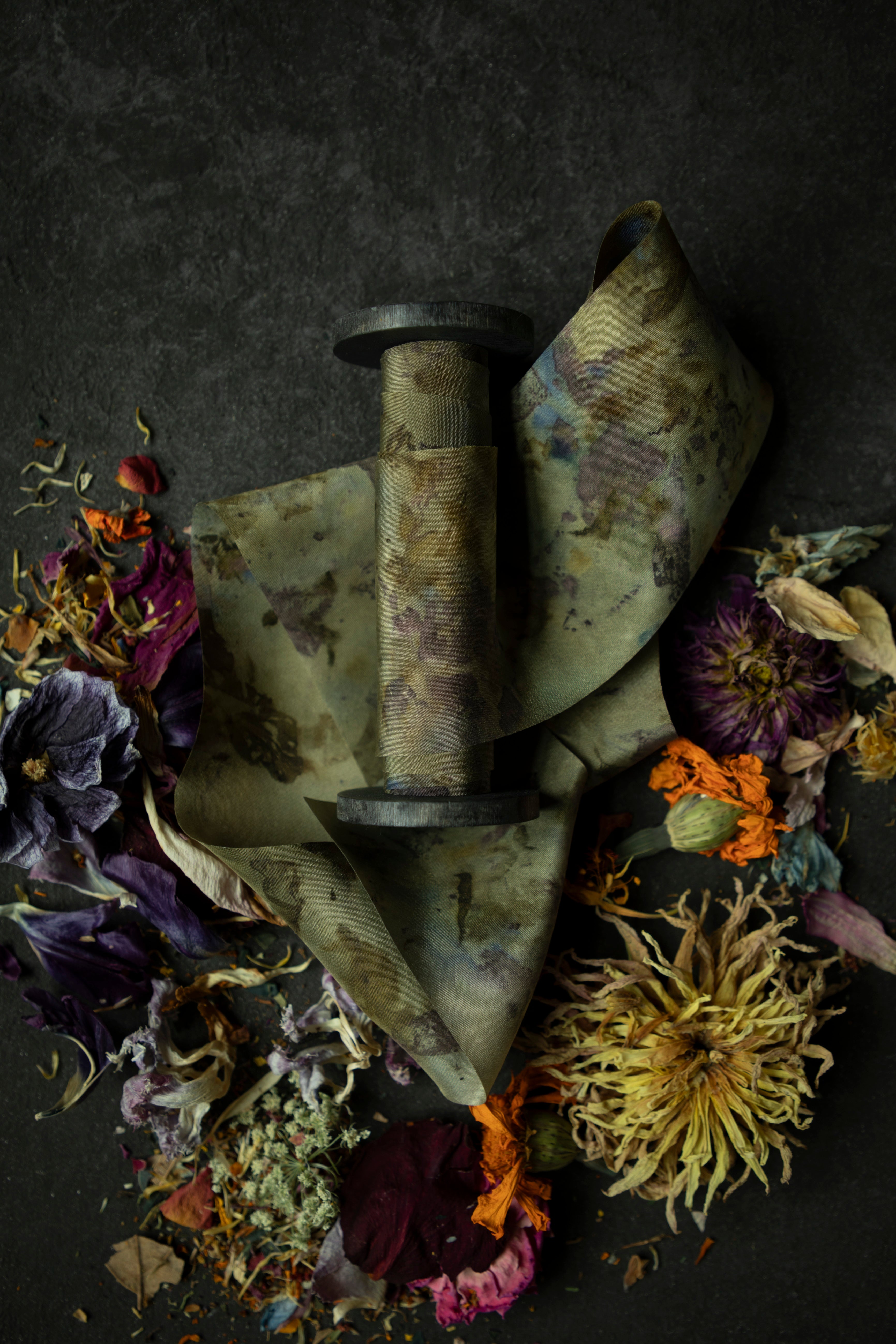 Limited-edition eco-print silk ribbon displayed on a wood spool surrounded by an assortment of dried flowers