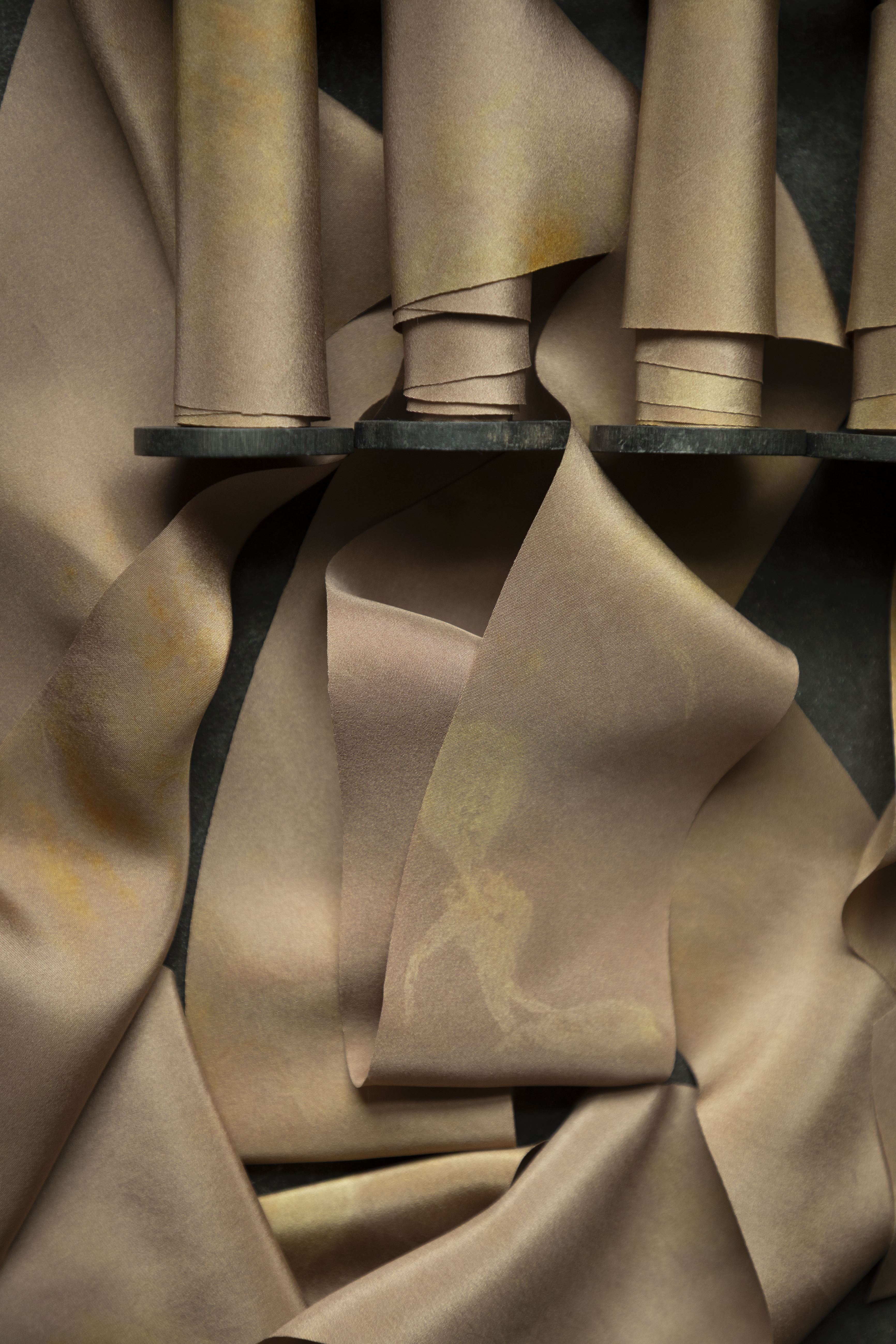 Close-up of silk ribbons on vintage wood spools with folds on a dark background