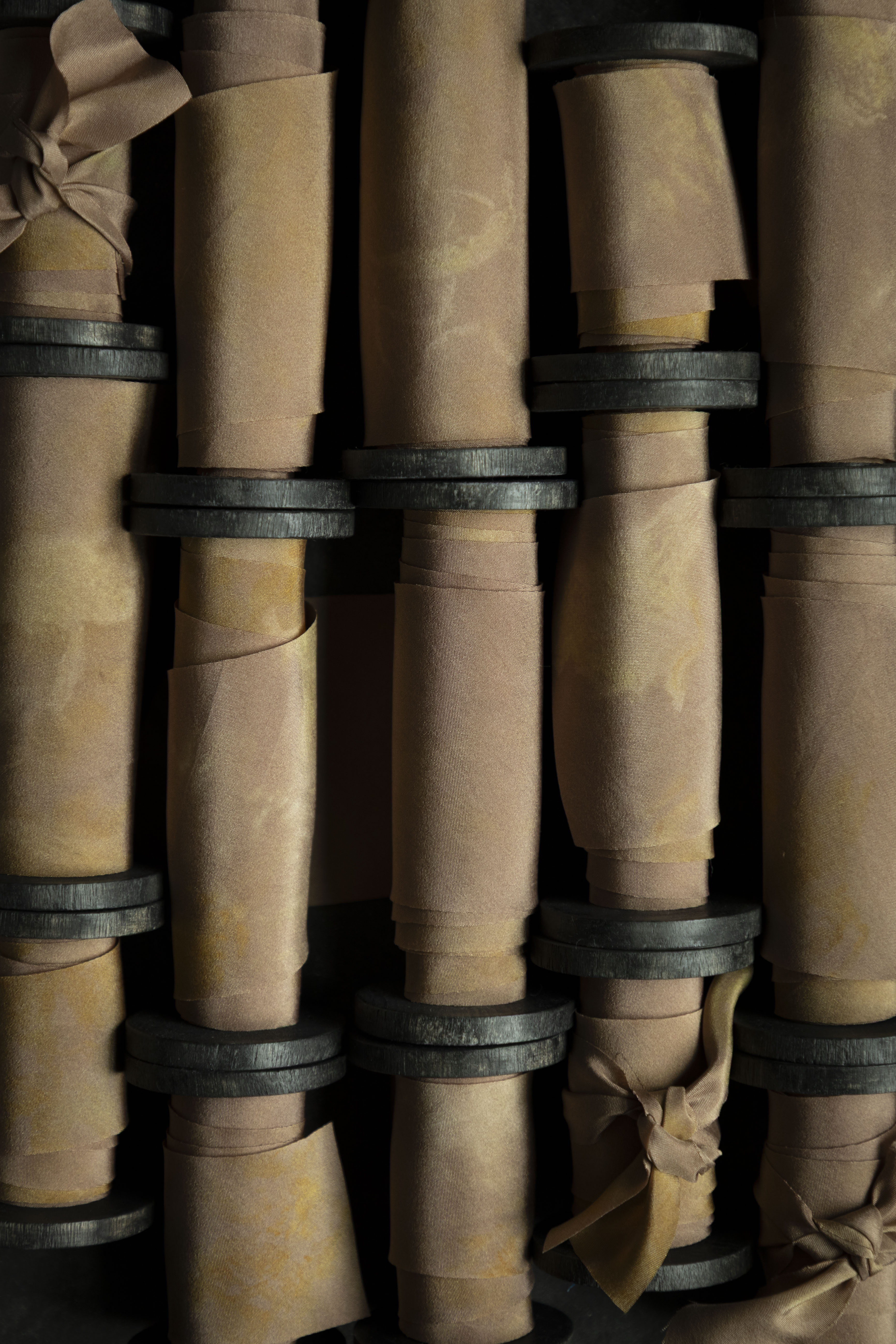 Close-up of hand-dyed silk ribbon on antique wood spools on a dark background