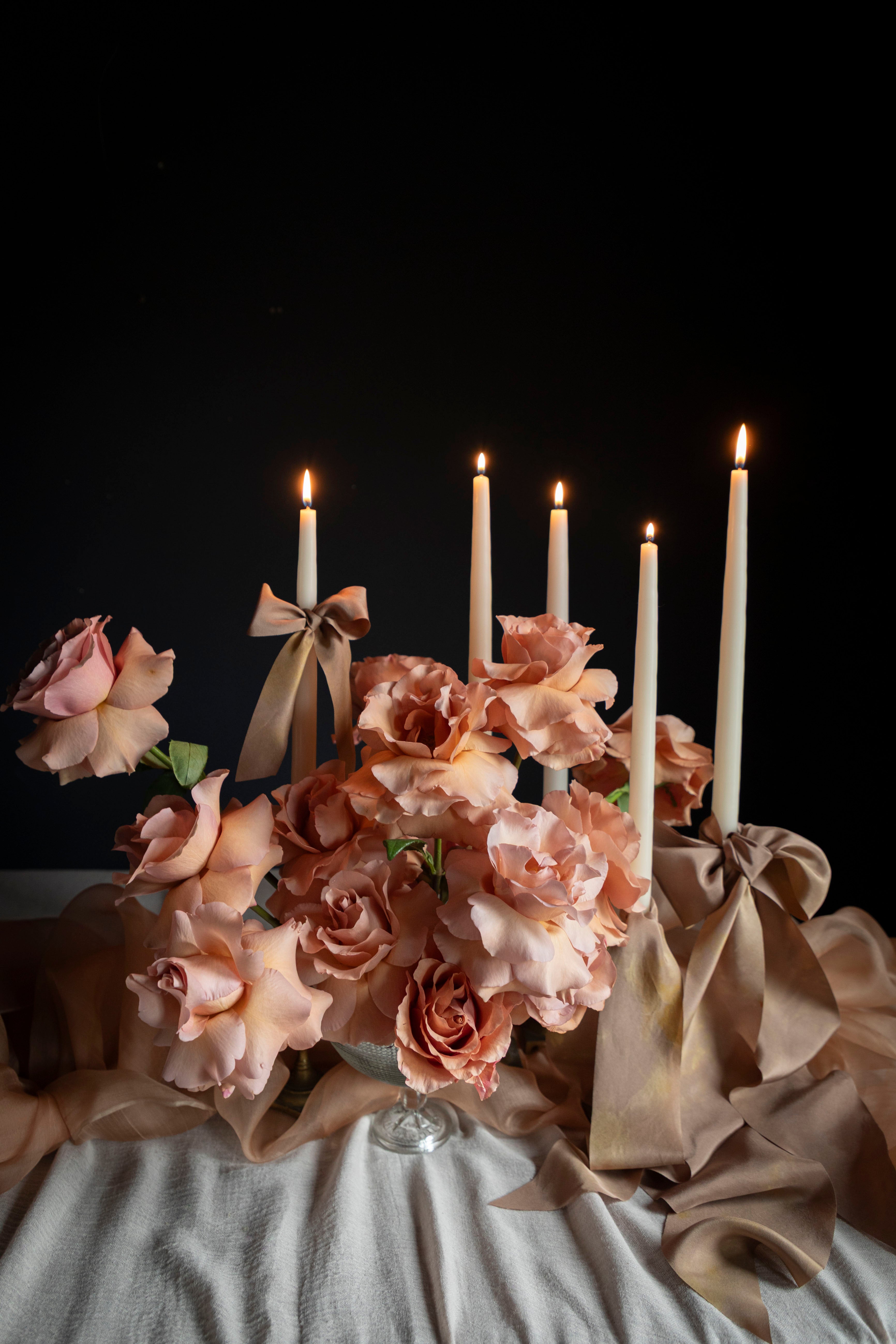 Decorative setup with flowers, candles, and ribbons on a dark background