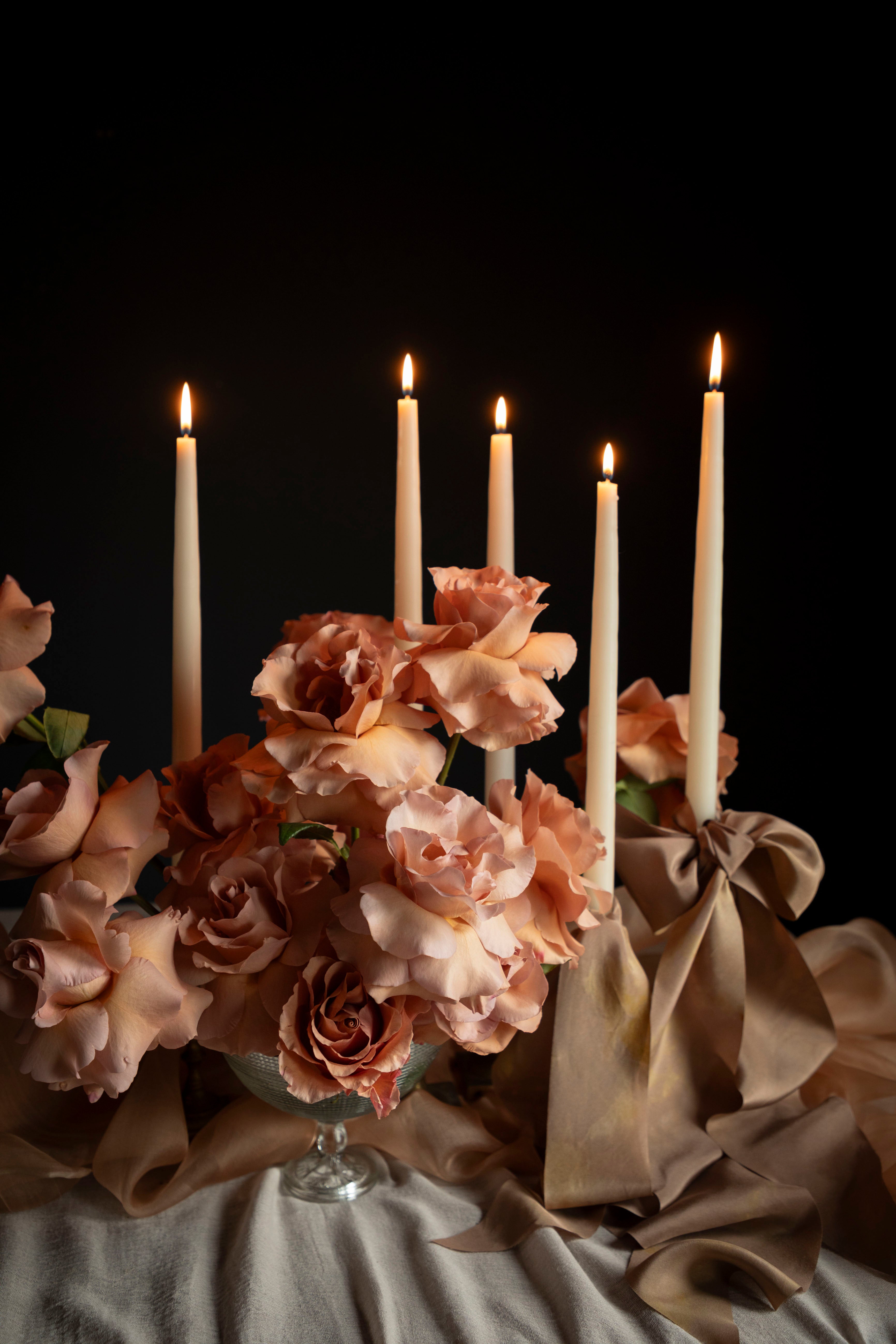Candlelit scene with flowers and draped fabric against a dark background