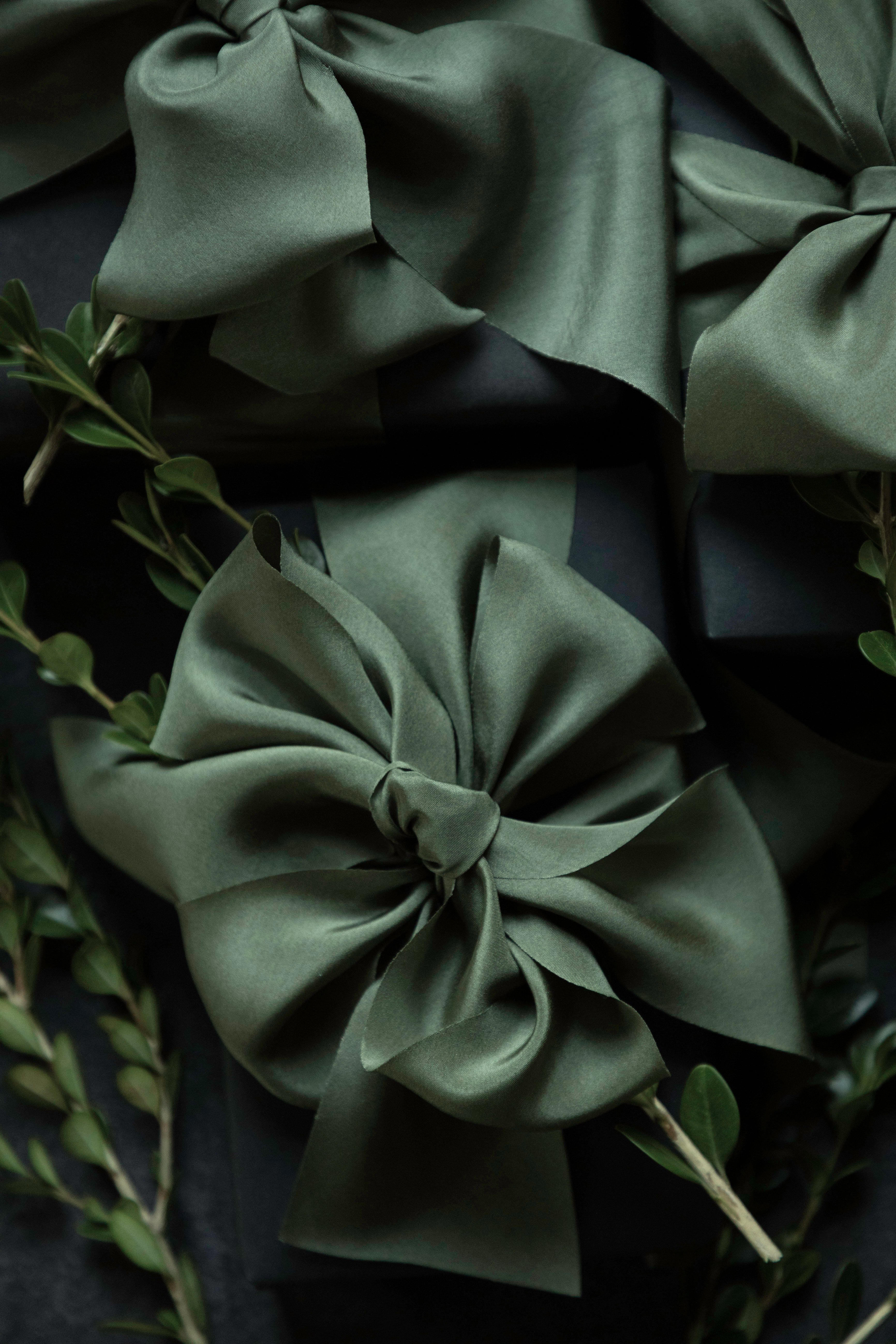 Olive green satin ribbon bows arranged on a dark background with green foliage accents.