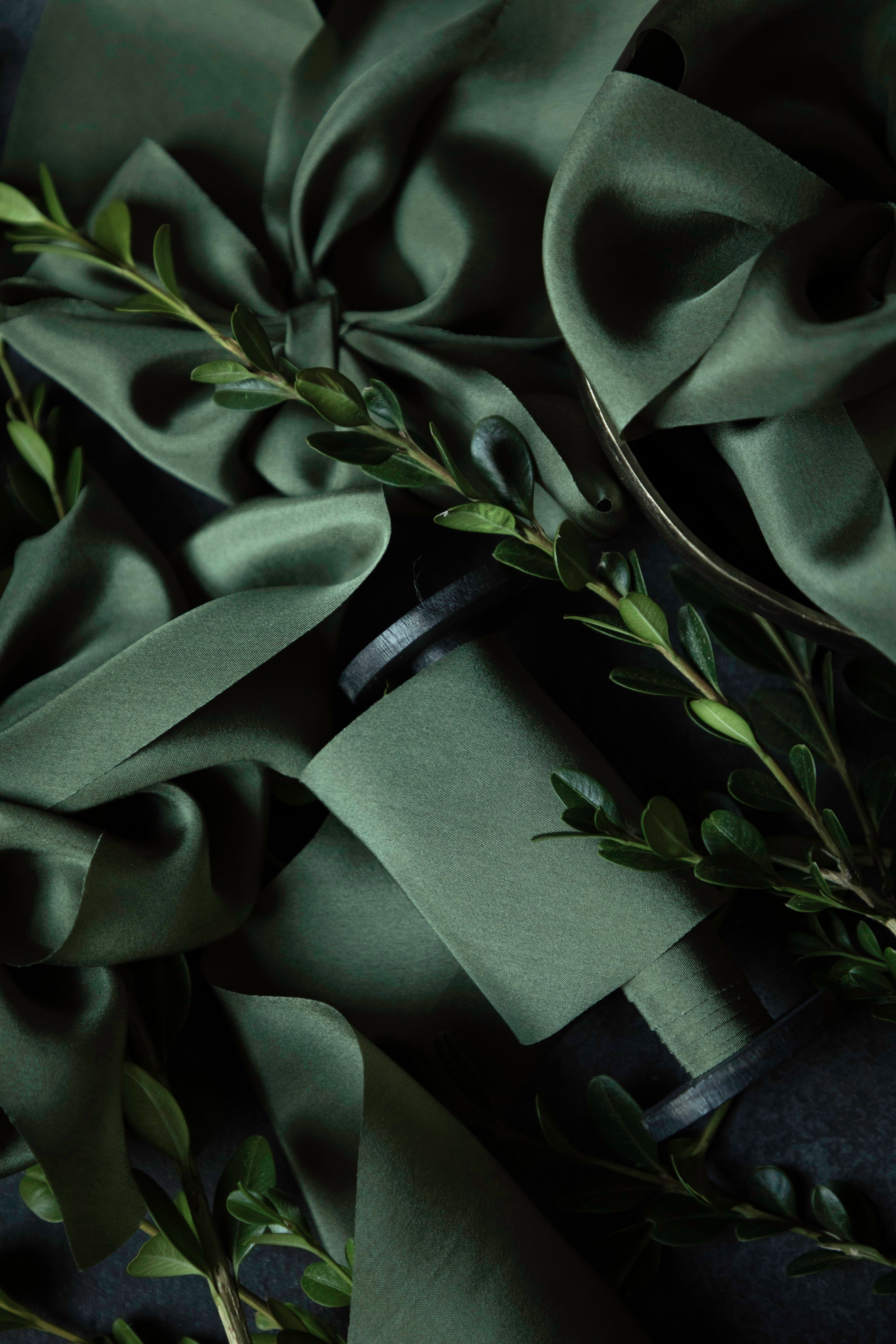 Dark green satin ribbon arranged with small green boxwood leaves on a dark background.
