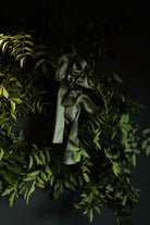 A dark olive green satin ribbon tied in a large bow and draped among green leaves against a very dark background.