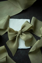 Green satin bow on a white napkin with additional green fabric around it on a dark surface.