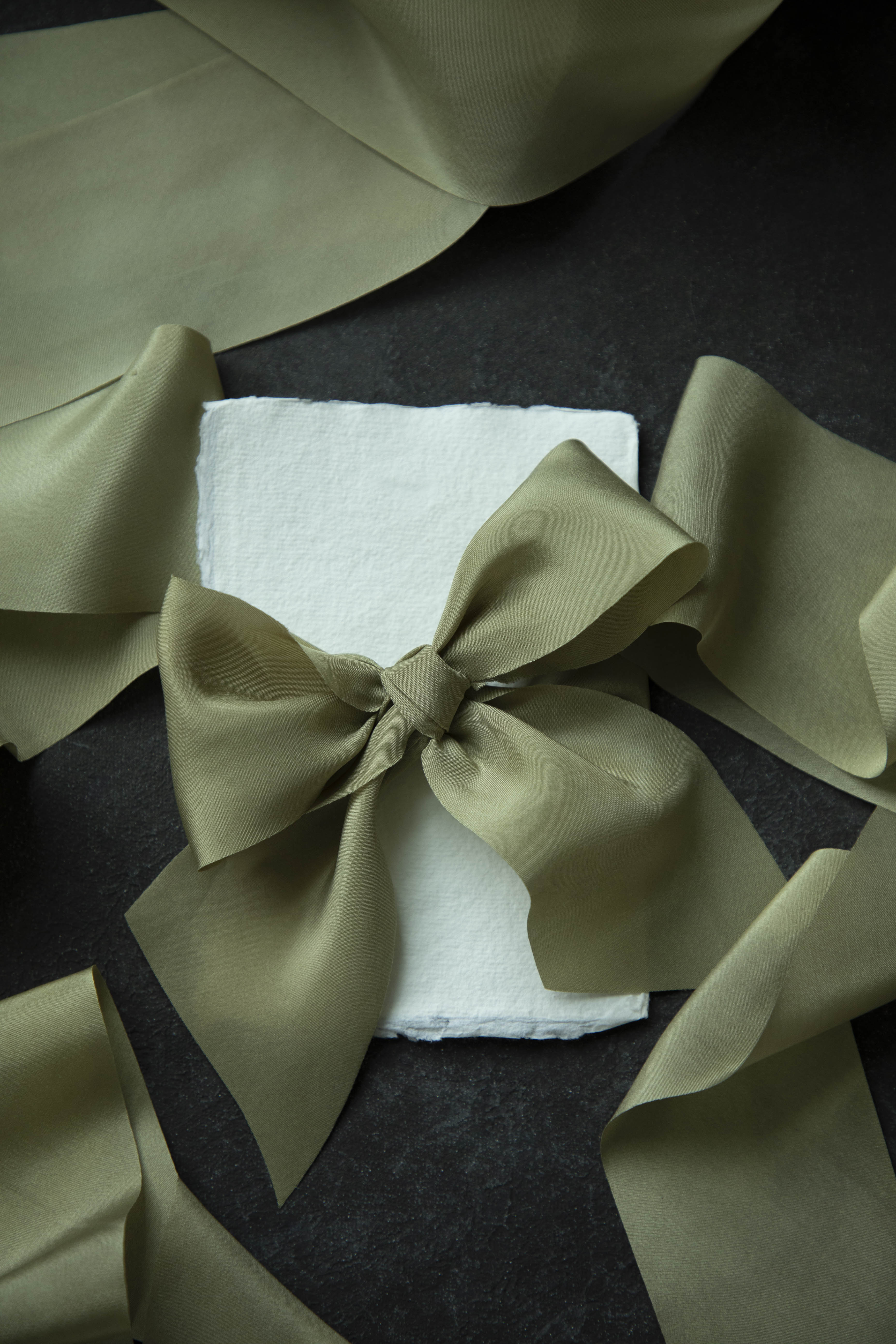Green satin bow on a white napkin with additional green fabric around it on a dark surface.