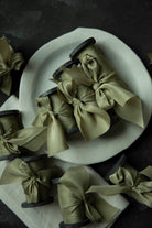Green ribbons tied into bows on wooden spools with a white plate in the background.
