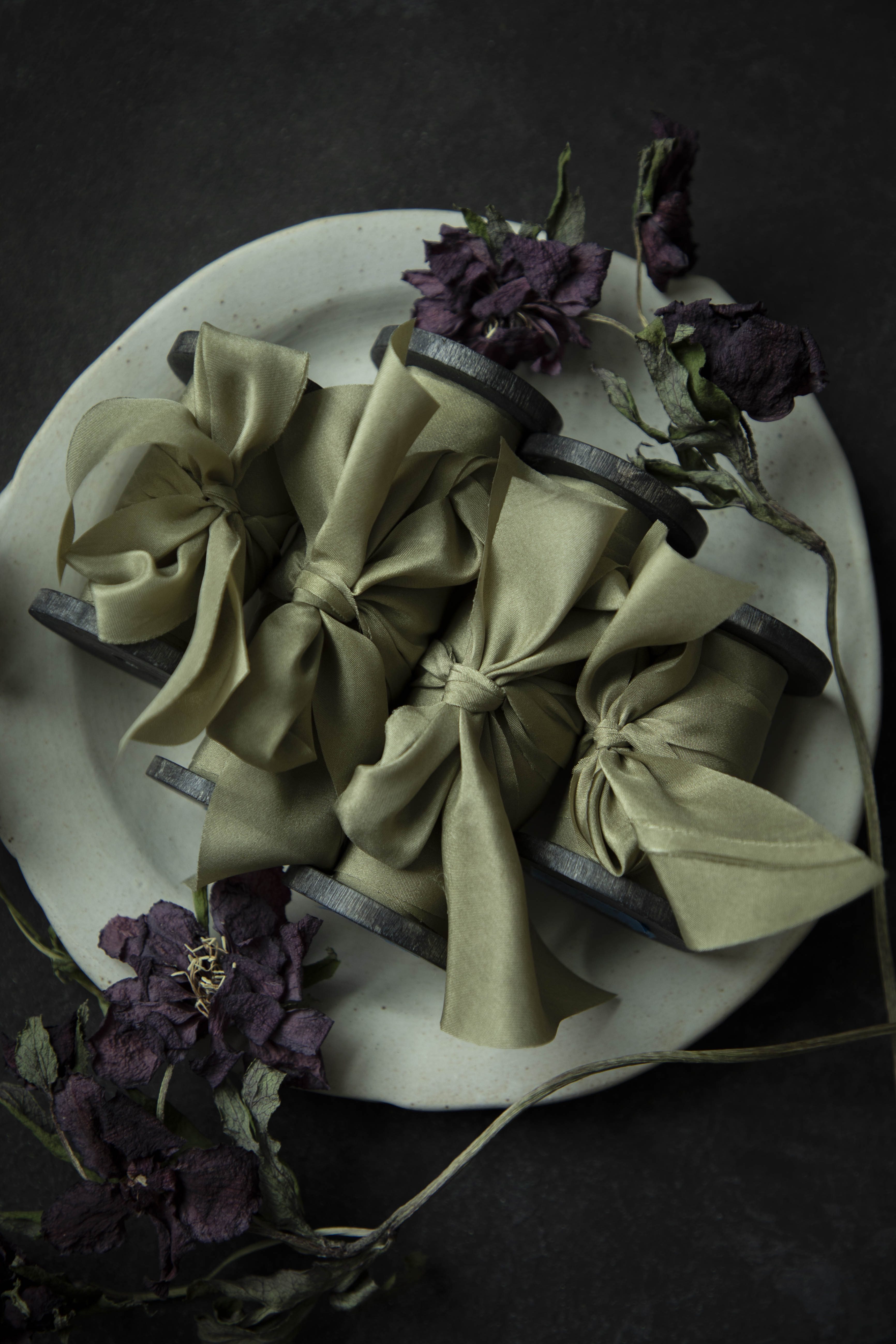 Green silk ribbons with dried hellebore flowers on a white plate on a dark background