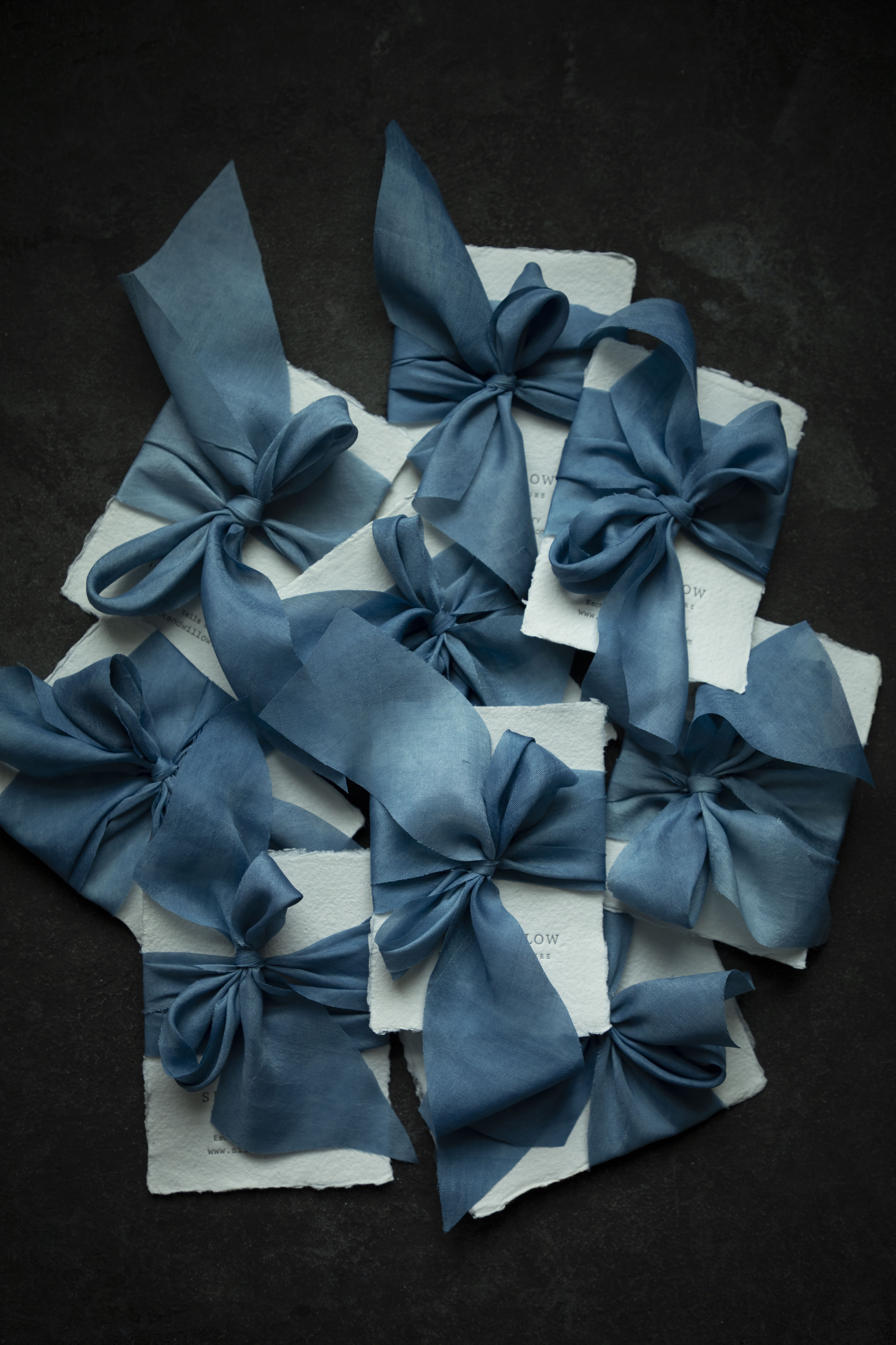 Indigo dyed Blue ribbon bows on white paper against a dark background