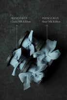 Three wood spools wrapped in pale blue sheer silk ribbon bows, arranged on a dark textured surface.