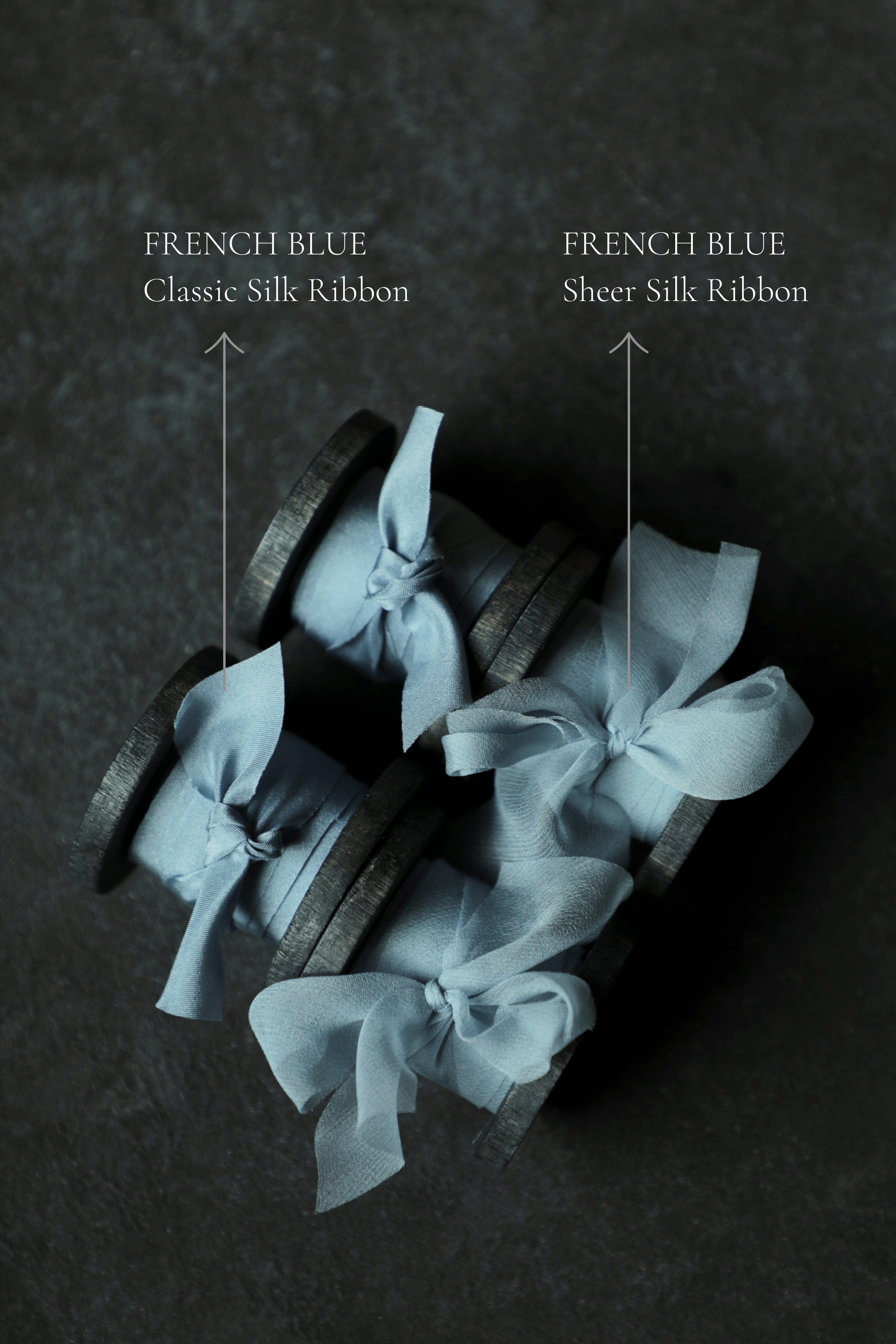 Three wood spools wrapped in pale blue sheer silk ribbon bows, arranged on a dark textured surface.