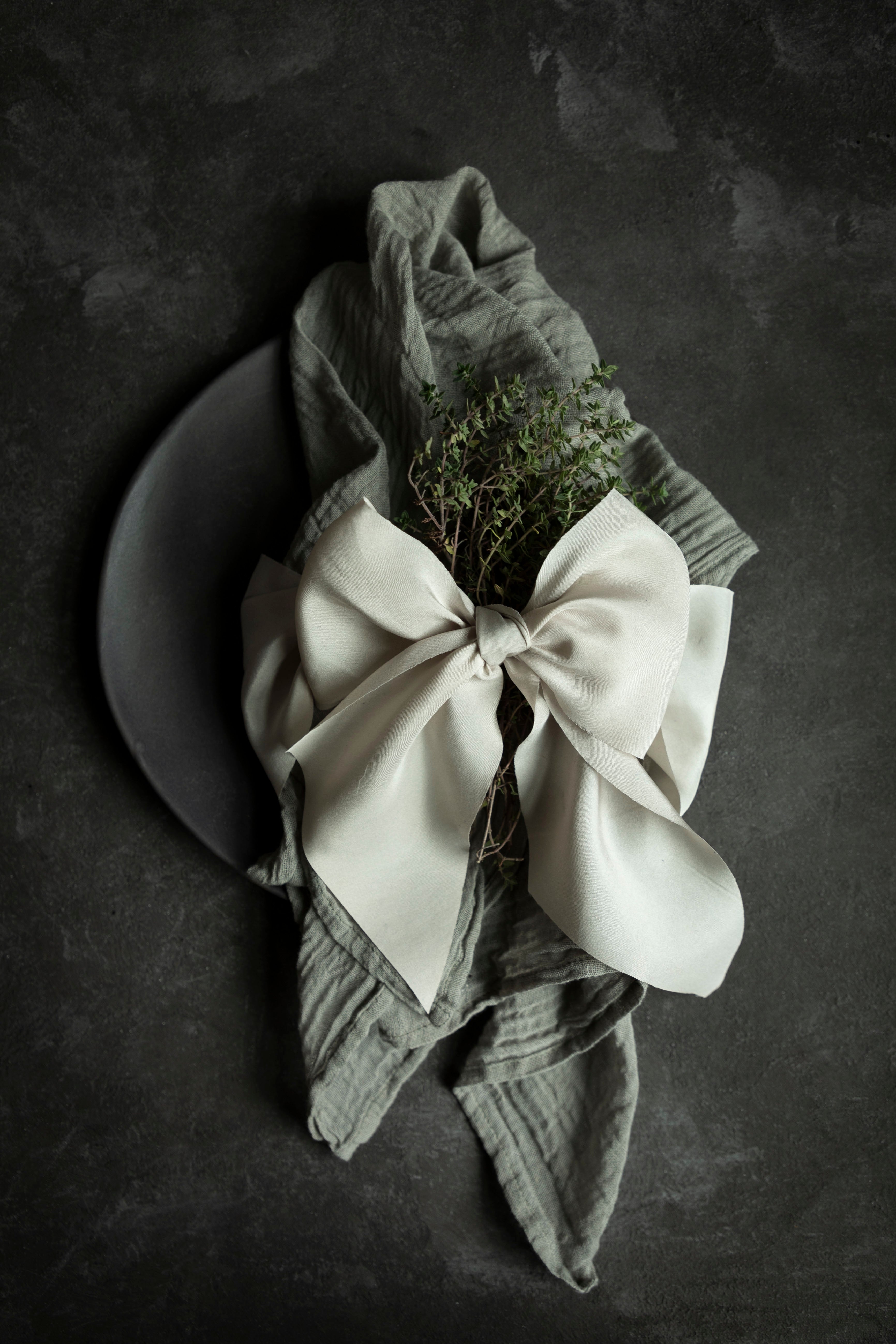 Folded napkin with a white bow and greenery on a dark surface