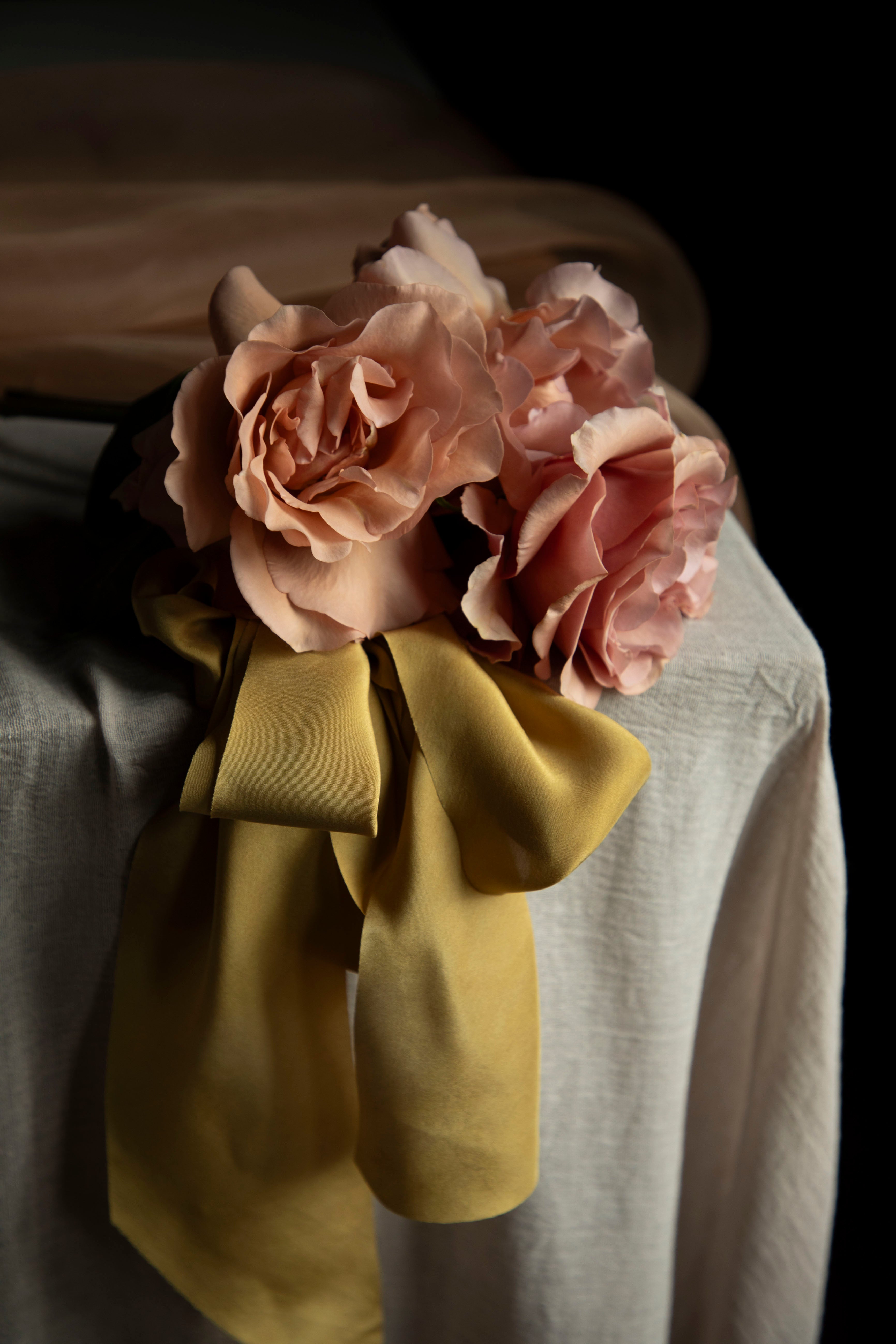 Floral arrangement with pink roses and a yellow bow on a neutral background