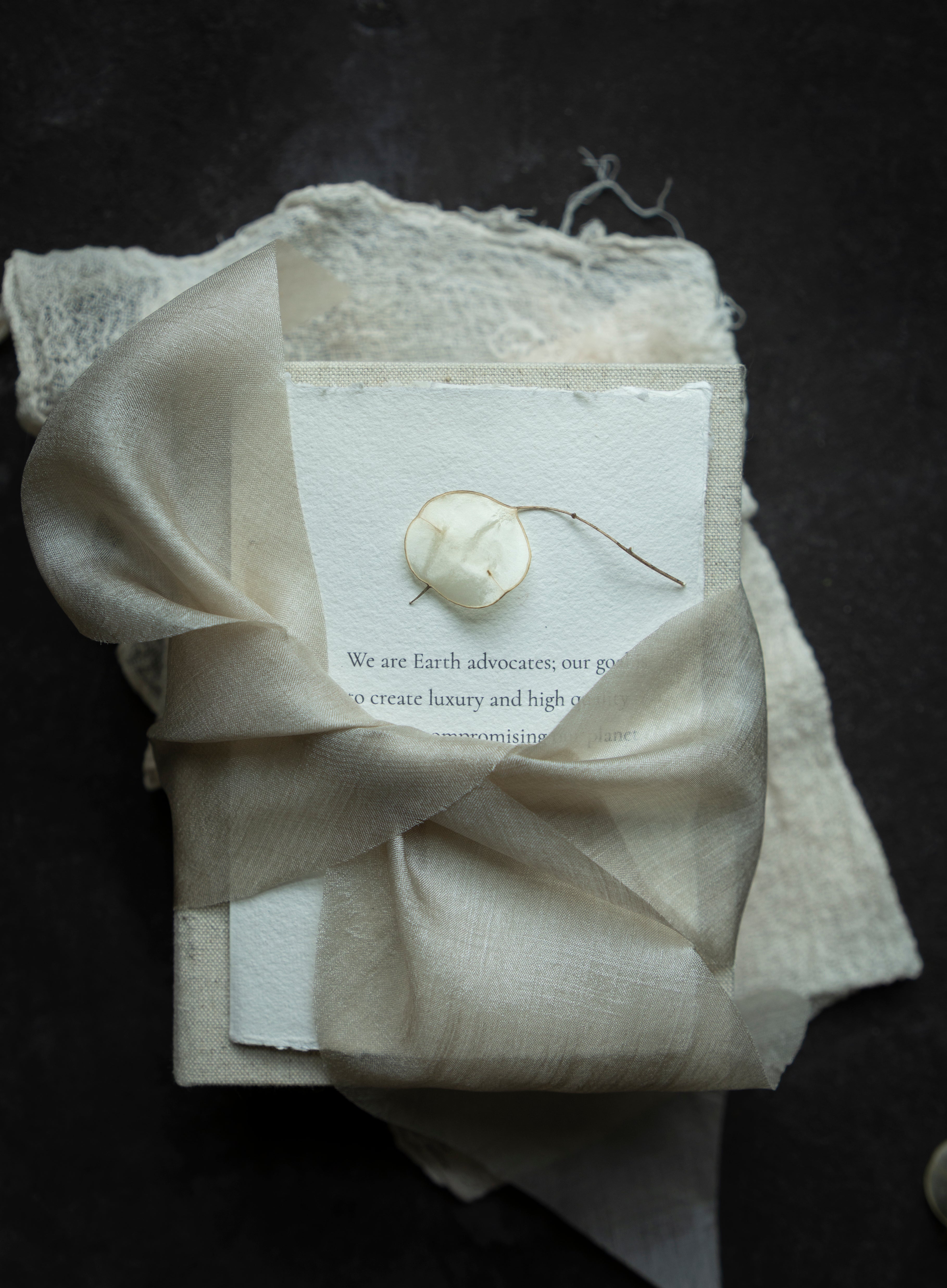 Neatly folded beige fabric with a dried plant and card on a dark background