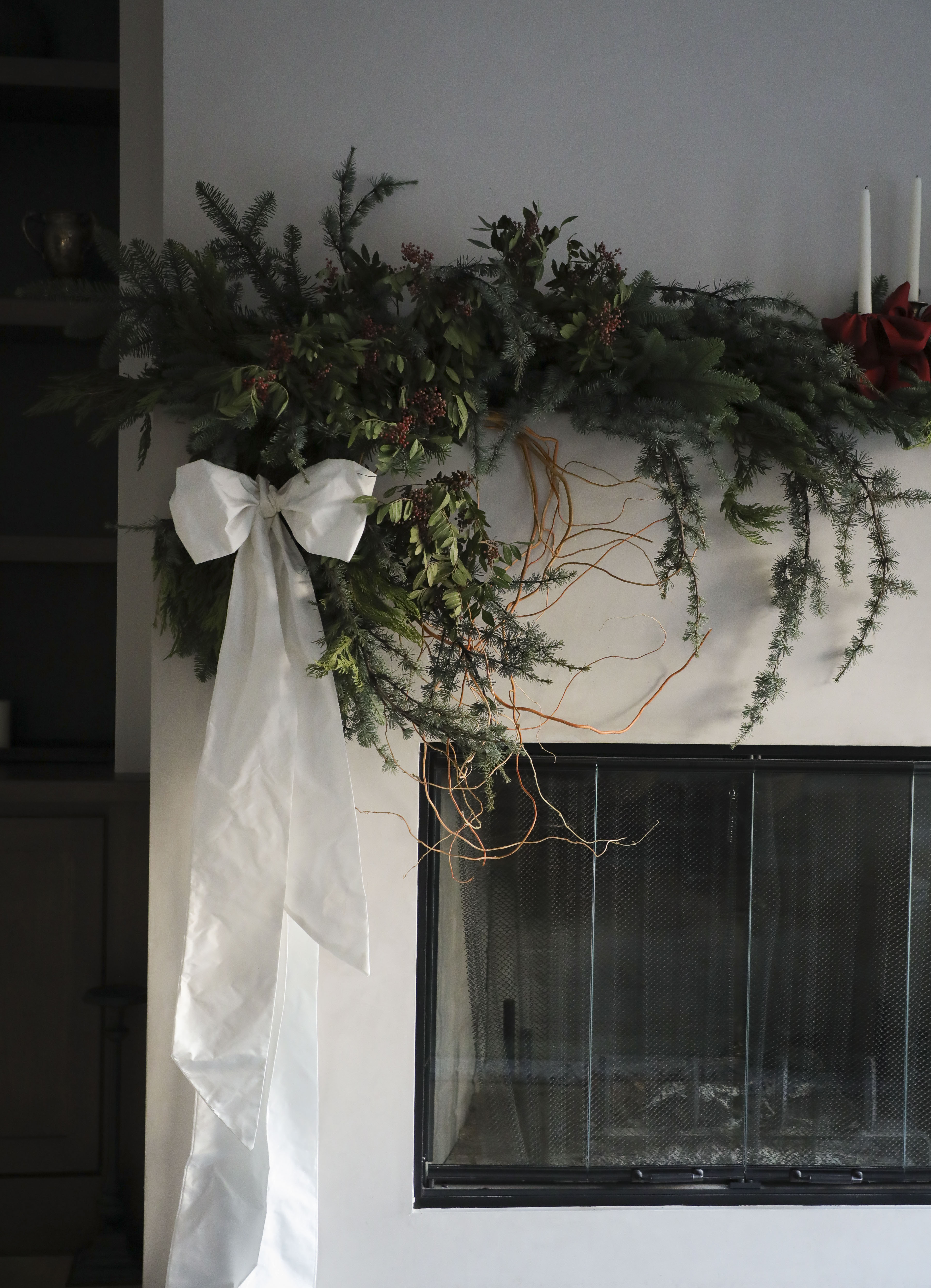 Decorative greenery on a mantel with a white ribbon and a fireplace in the background.