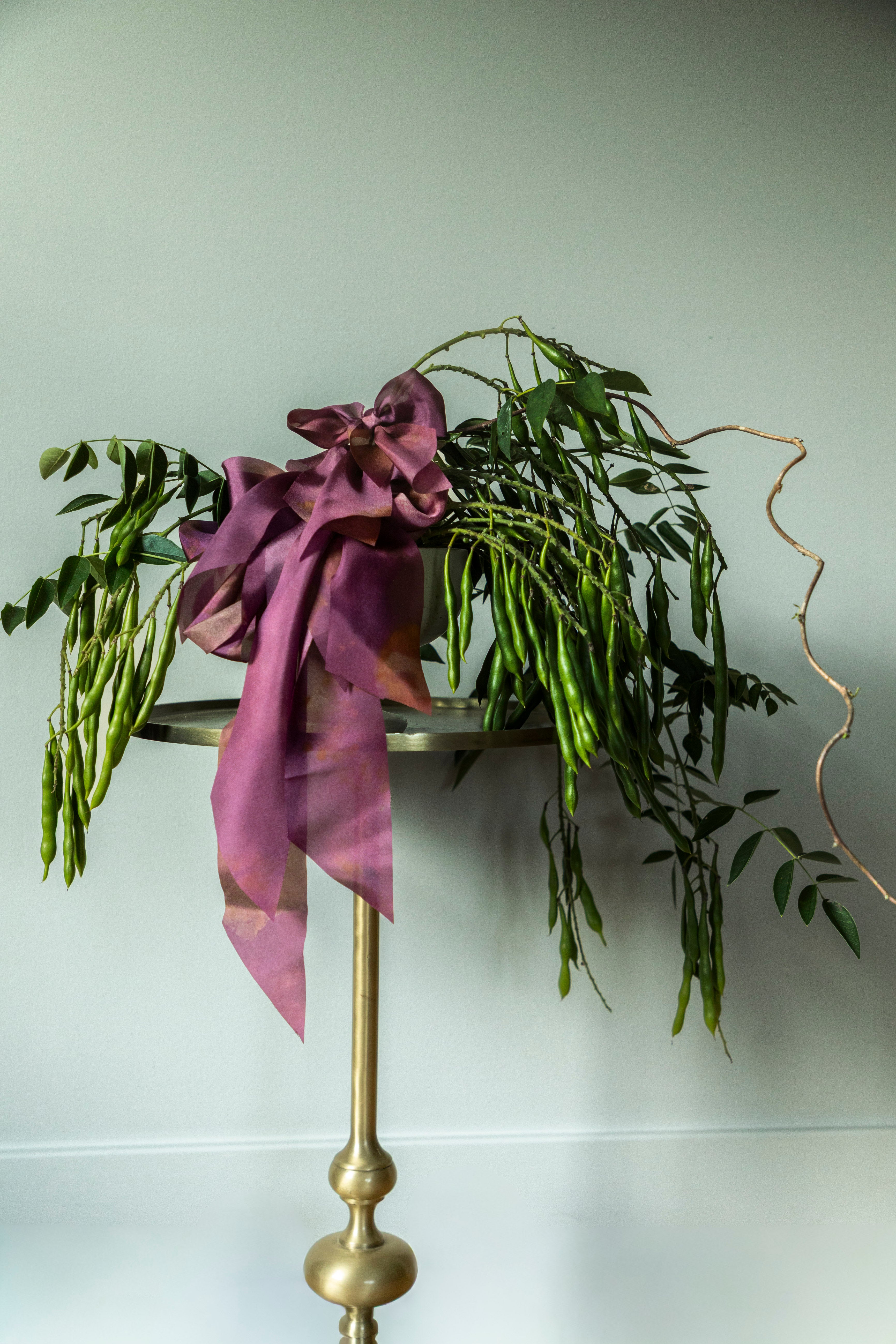 Decorative stand with greenery and a purple ribbon against a white background
