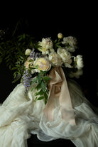 Floral arrangement with white flowers and green leaves draped over a white fabric against a dark background. highlighting the best wedding silk ribbon in blush color.