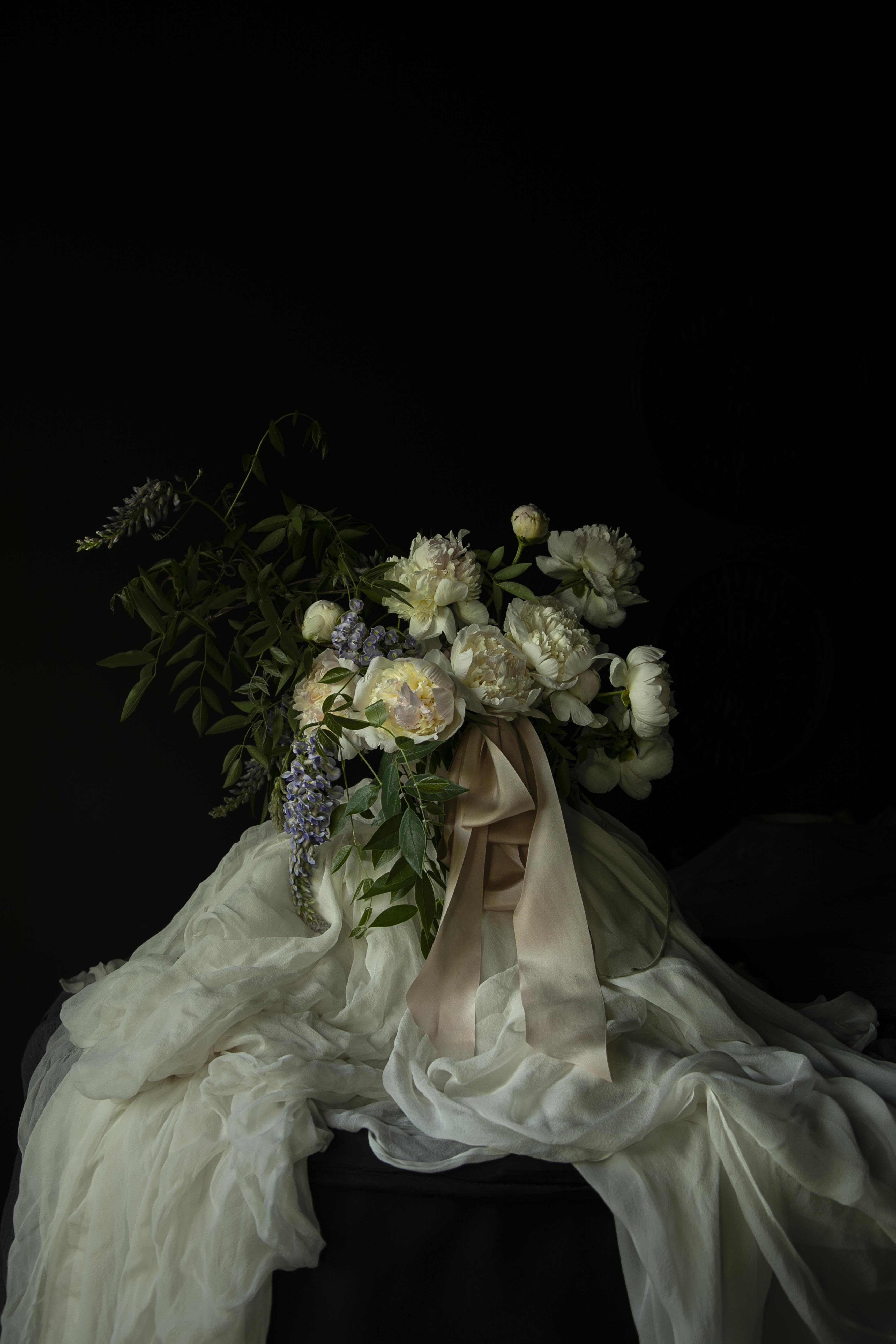 Bouquet of peony flowers tied with blush silk ribbon on antique white silk fabric against a black background