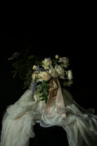 Bouquet of peony flowers tied with blush silk ribbon on antique white silk fabric against a black background