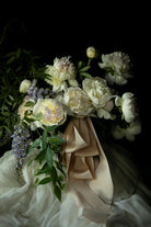 Bouquet of white flowers with greenery and blush silk ribbon against a dark background. dutch master mood for weddings.