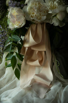 Close-up of a bouquet with white flowers and blush silk ribbons, with a dark, moody background