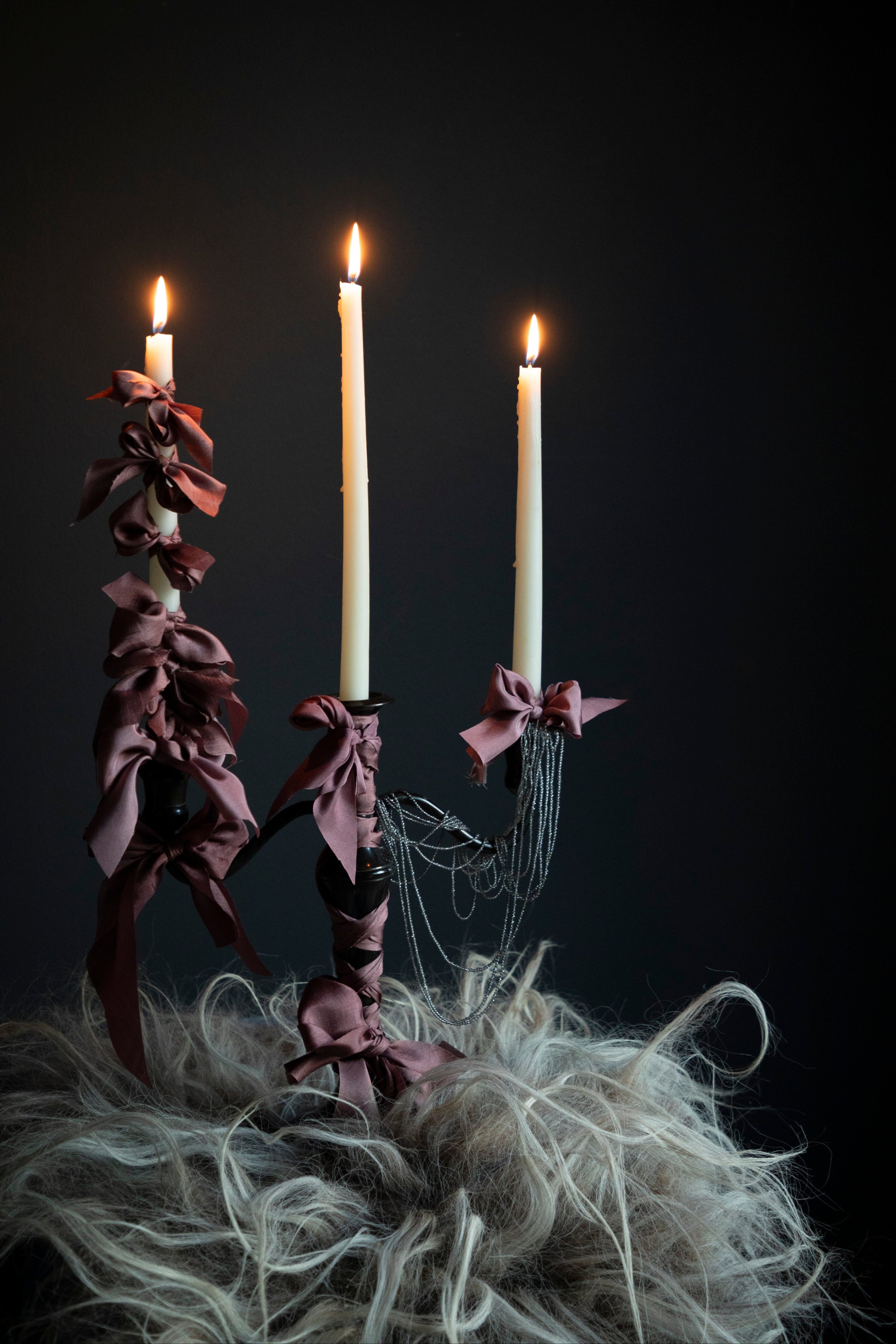 candle holder witth silk ribbon bows against a dark background. moody viking feel.