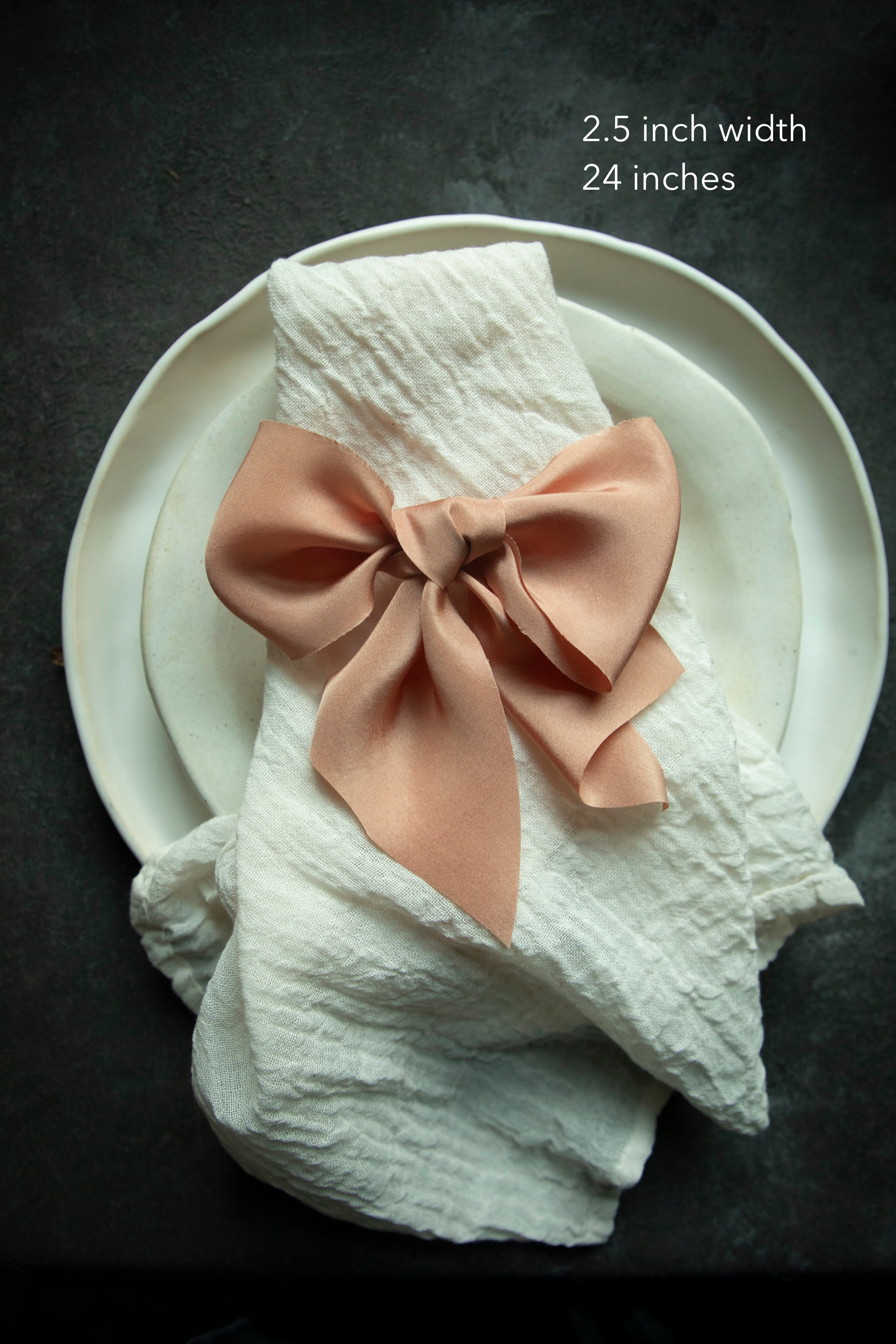 An elegant soft coral organic loomed silk ribbon tied into a bow on a cotton napkin, highlighting intricate details for creating the perfect ribbon bow. Ideal for wedding accents such as bridal bouquets, invitation wraps, and table decor.
