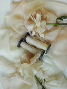 Close-up of a ribbon spool of blush-colored ribbon with a white flower on a white background