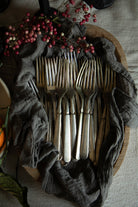 A set of vintage silver forks arranged in a wooden bowl draped with a dark gray cloth, decorated with red berries on a neutral fabric background.