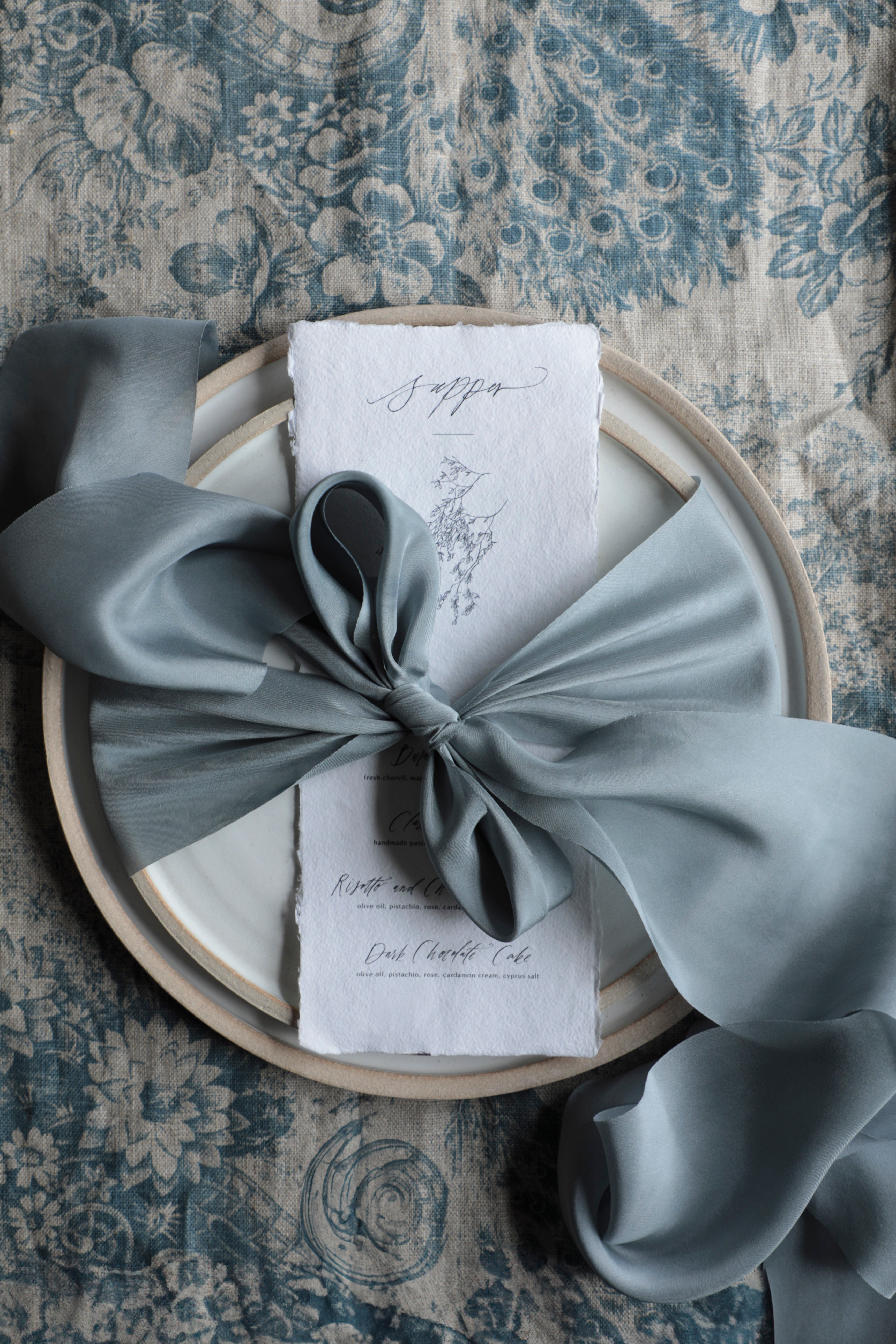 blue bow on a white napkin with text, placed on a textured surface.