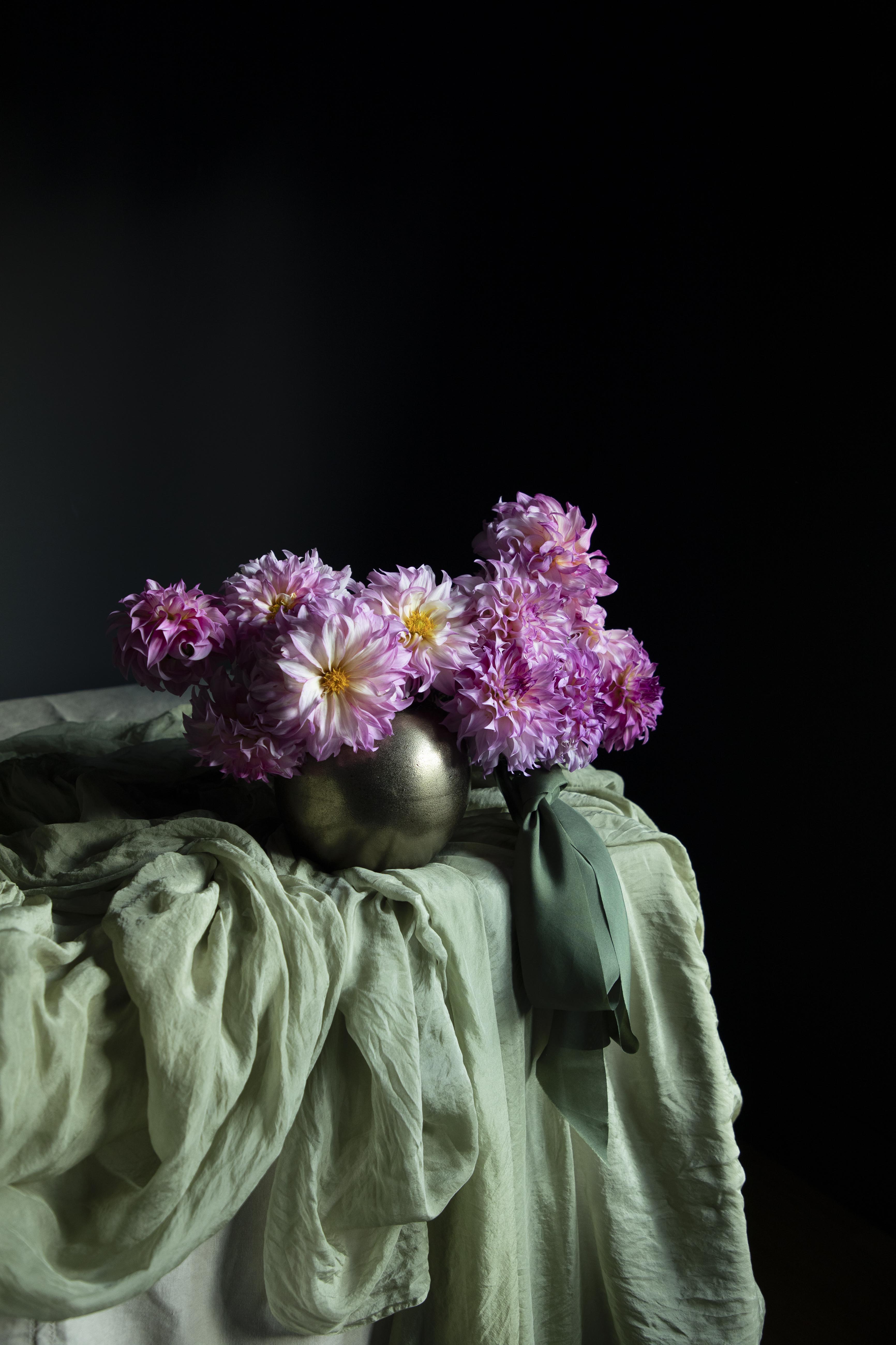 Vase with purple flowers on a draped surface against a black background
