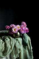 Vase with purple flowers on a draped surface against a black background