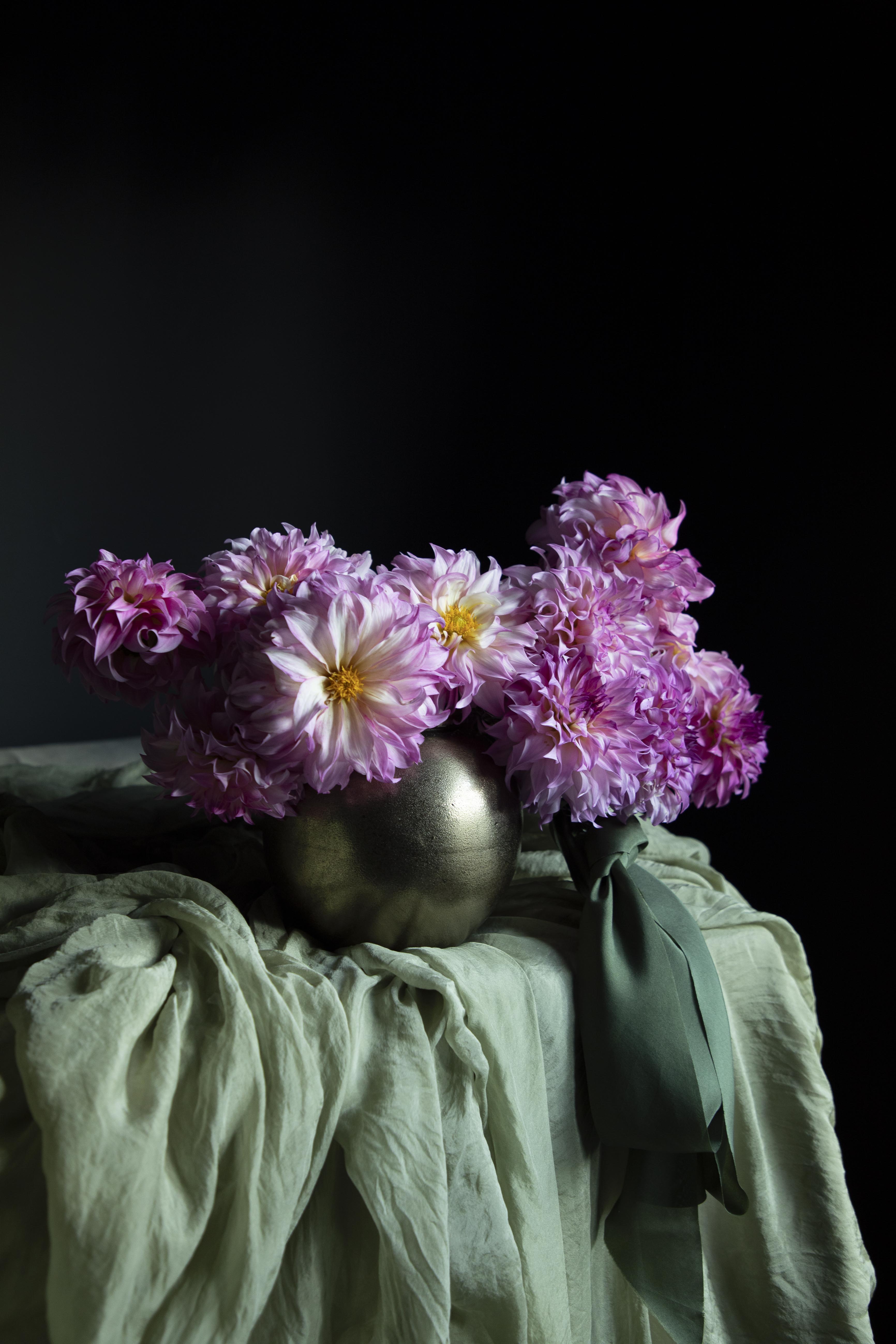 Pink flowers in a metallic vase on a green cloth with a dark background