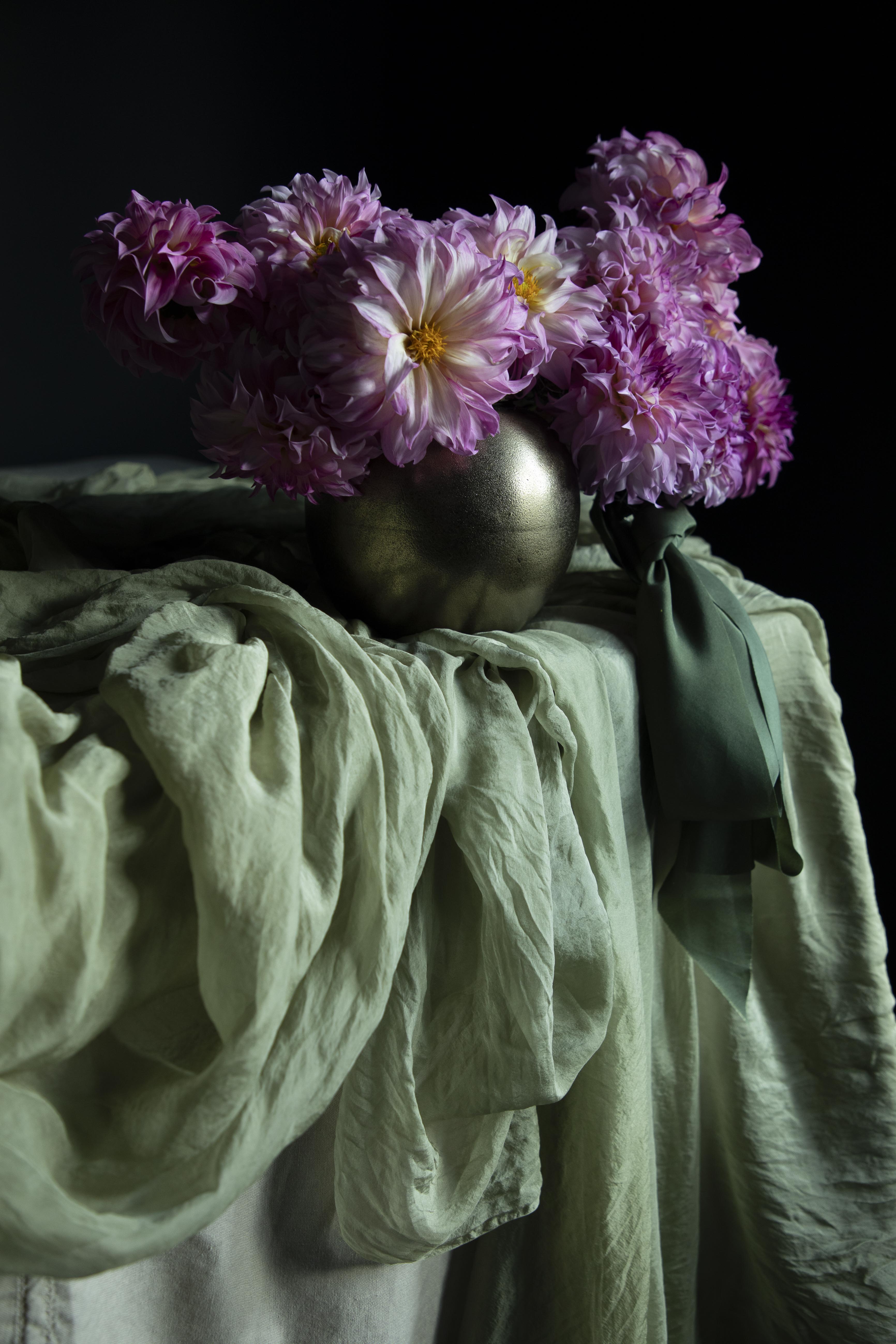 Purple flowers in a metallic vase on a draped silk fabric surface with a dark background