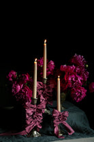 opalite aesthetic. Candle holder with purple ribbons and candles surrounded by pink peony flowers on a dark background. wedding table inspiration