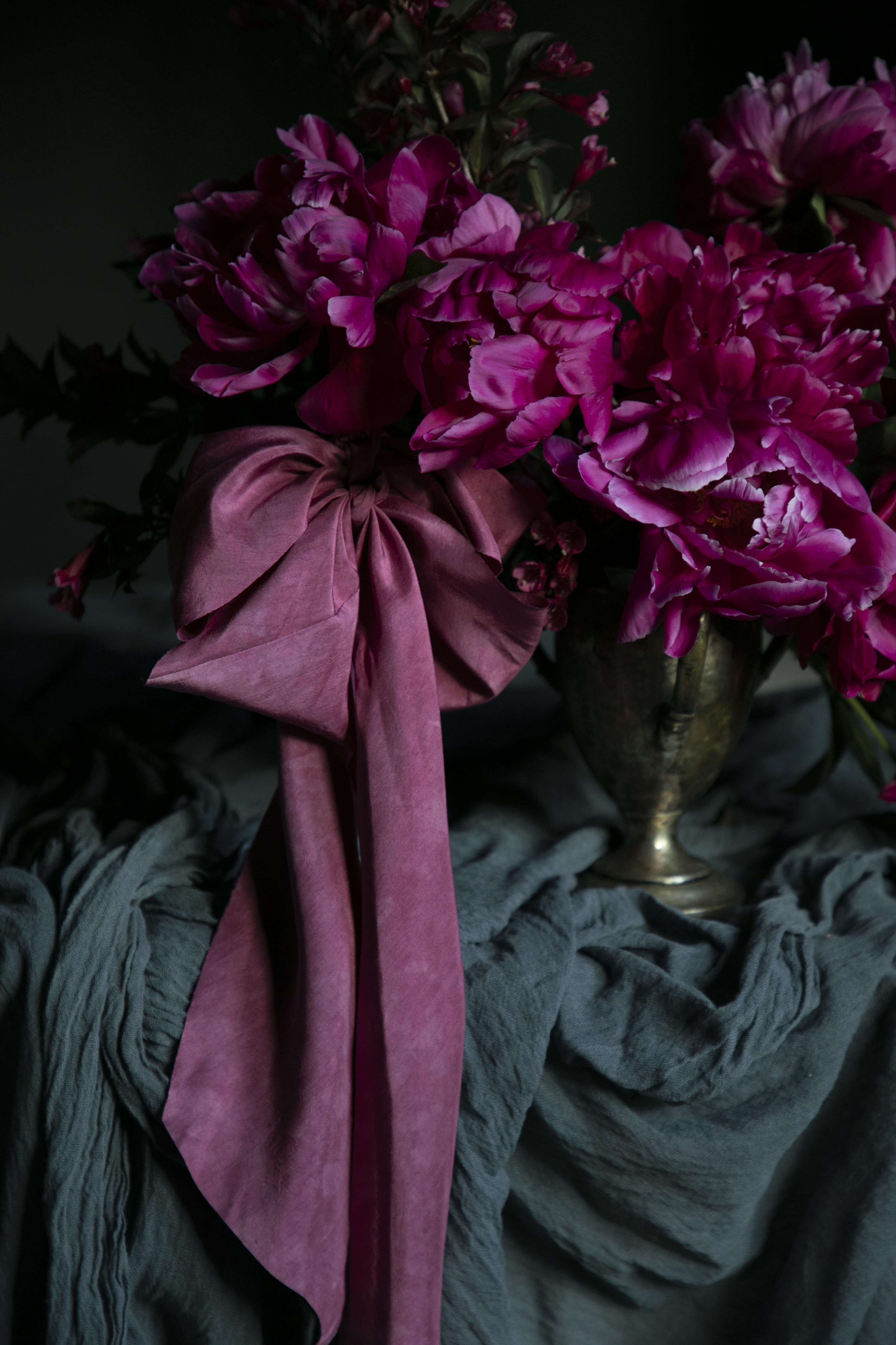 Pink flowers with a large pink bow in a silver vase on a dark background. opalite aesthetic.