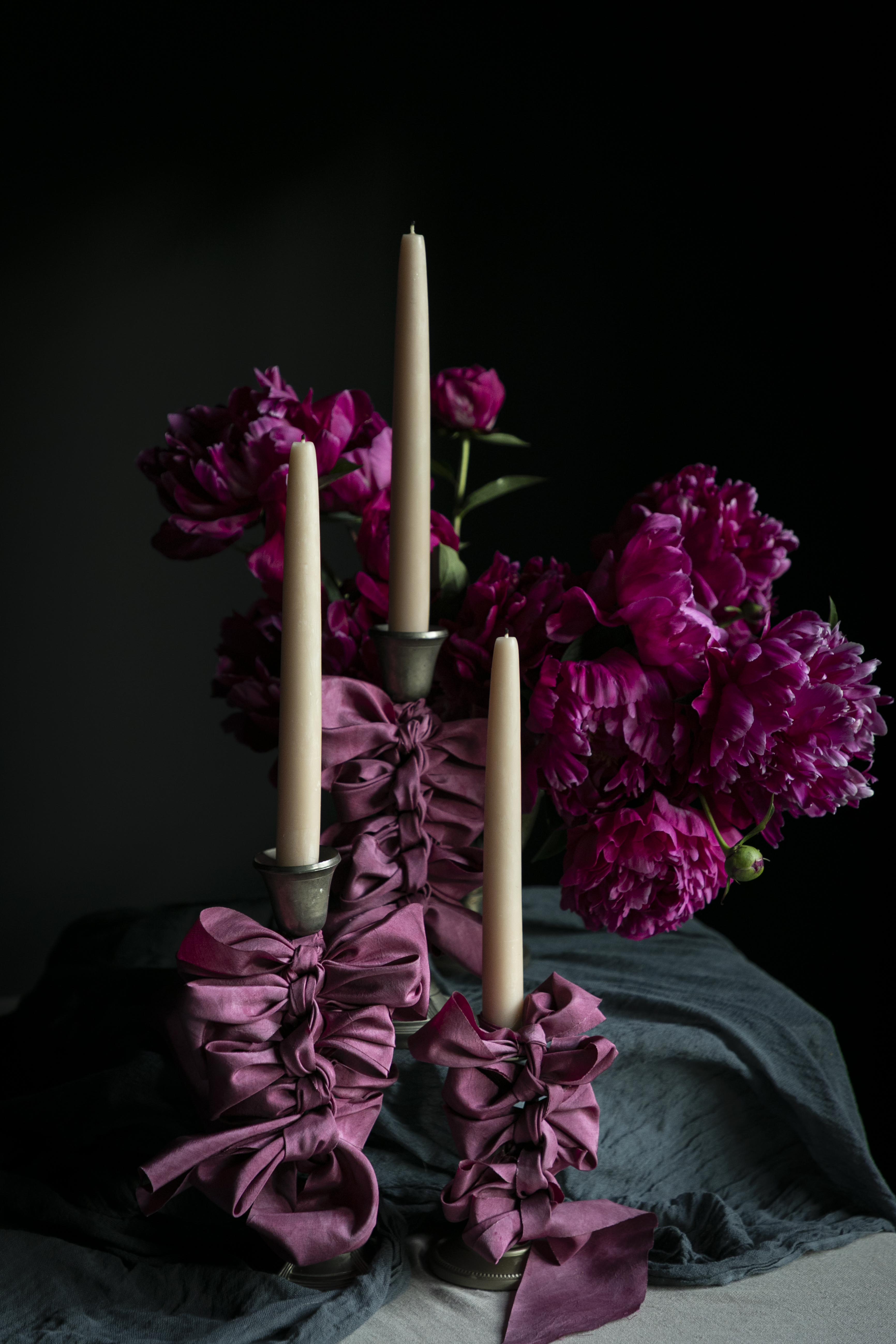 Candle holder with purple ribbons and candles in front of pink flowers on a dark background
