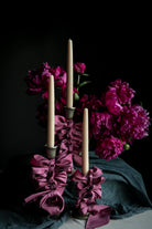 Candle holder with purple ribbons and candles in front of pink flowers on a dark background