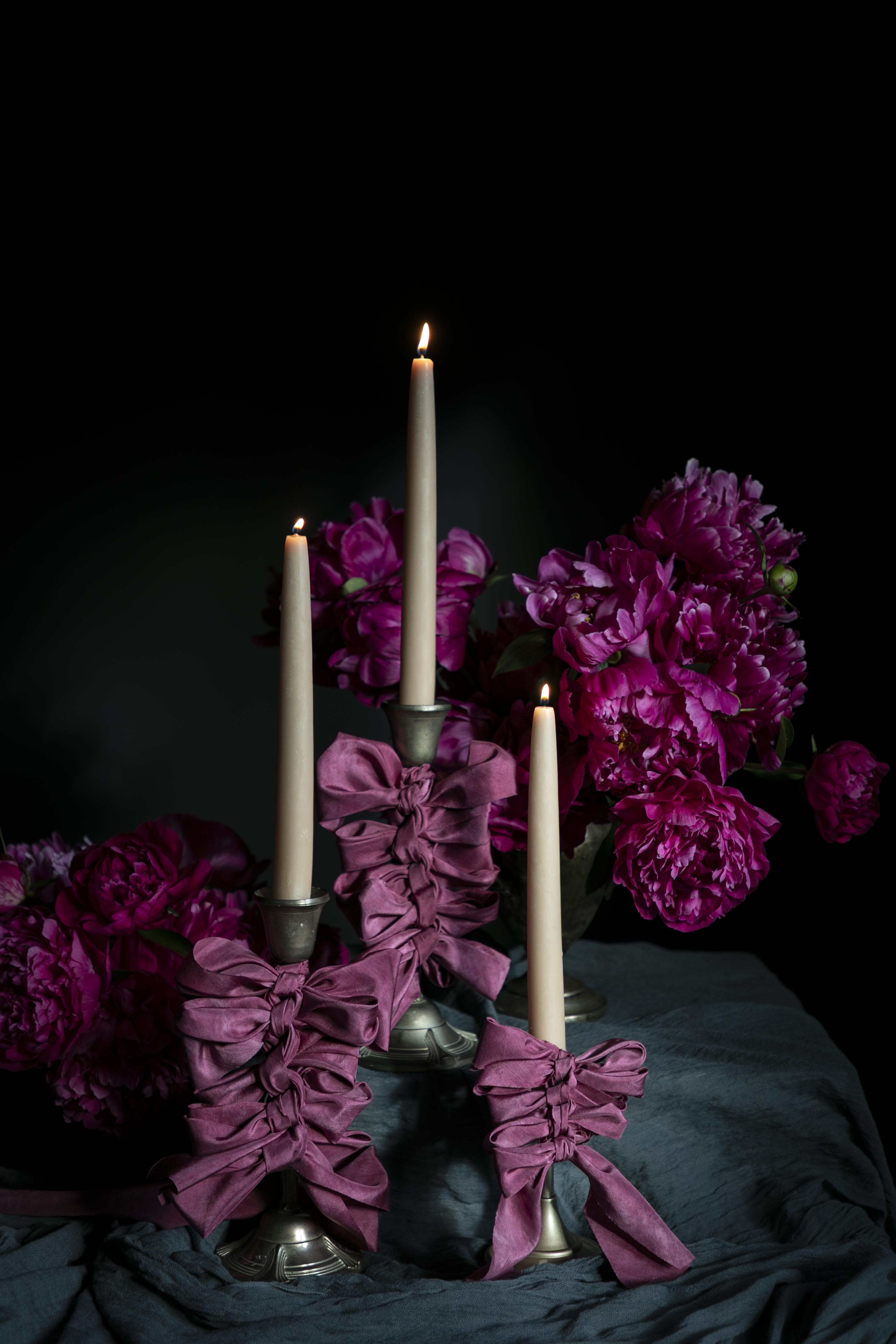 opalite aesthetic. Decorative candle holder with purple-pink ribbons and candles against a dark background.