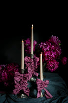 opalite aesthetic. Decorative candle holder with purple-pink ribbons and candles against a dark background.