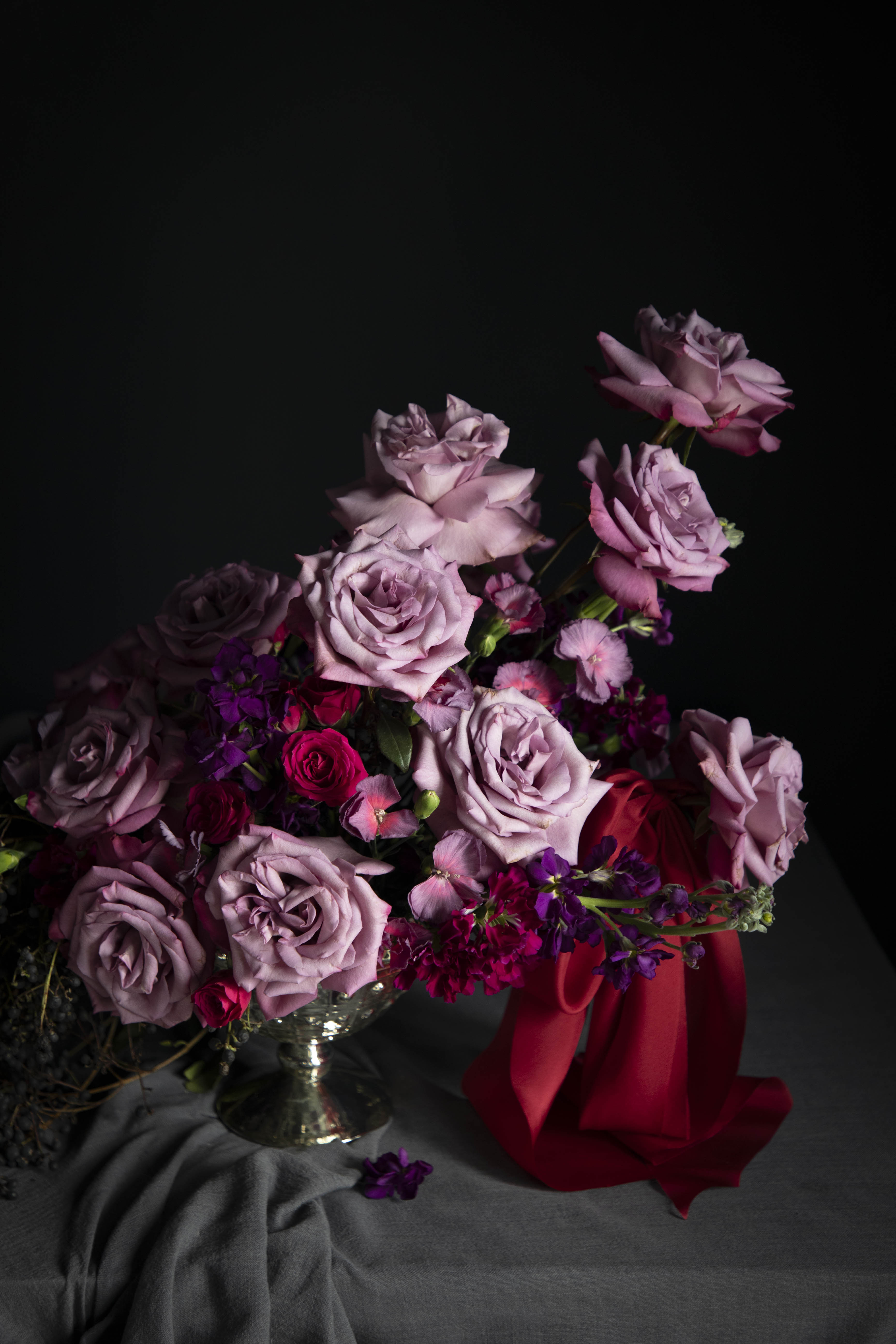 Bouquet of purple and pink roses with a red ribbon on a dark background