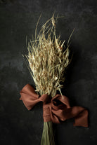 Bouquet of dried grasses tied with a copper colored silk ribbon on a dark background