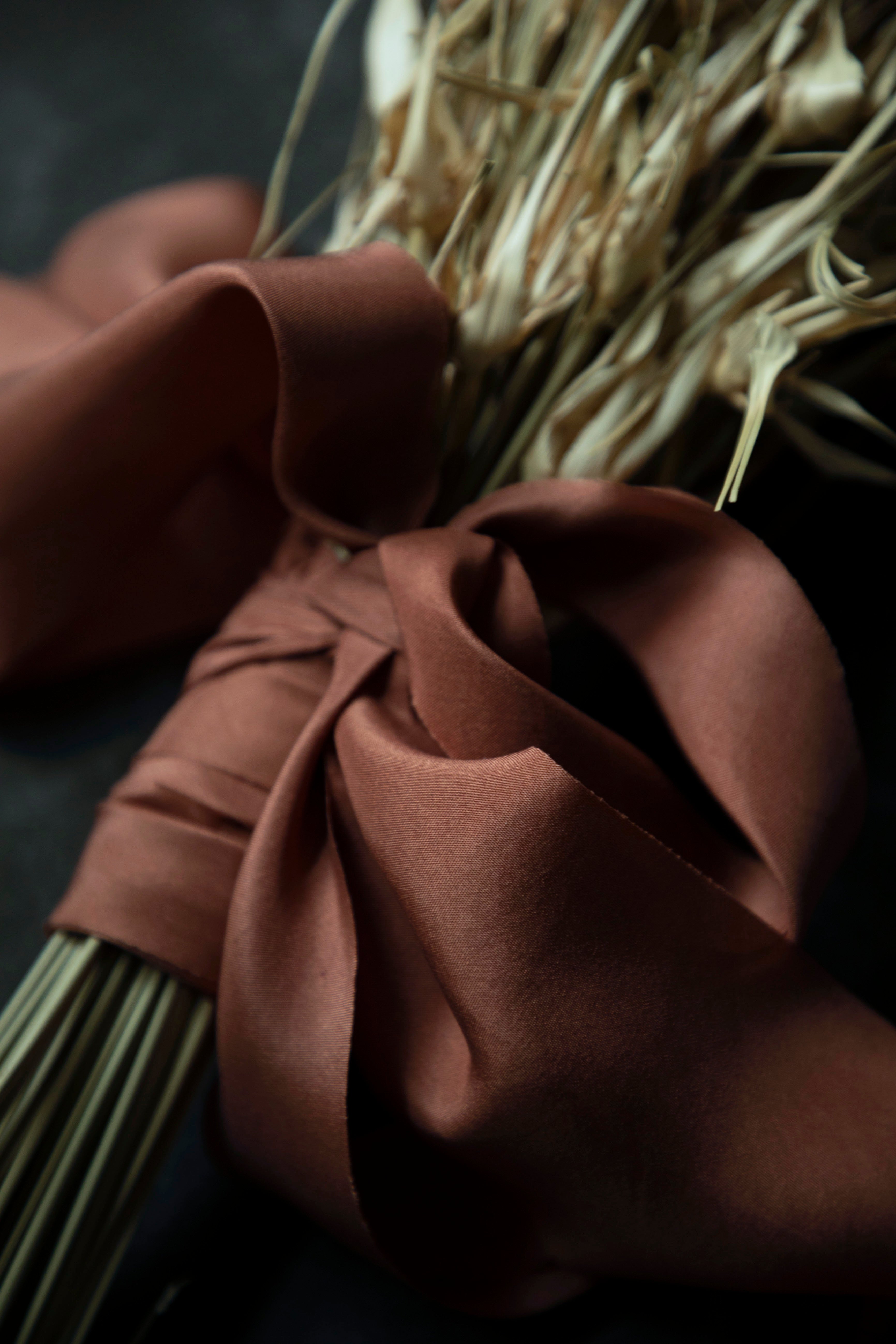Copper colored silk ribbon around a bundle of dried plants on a dark background