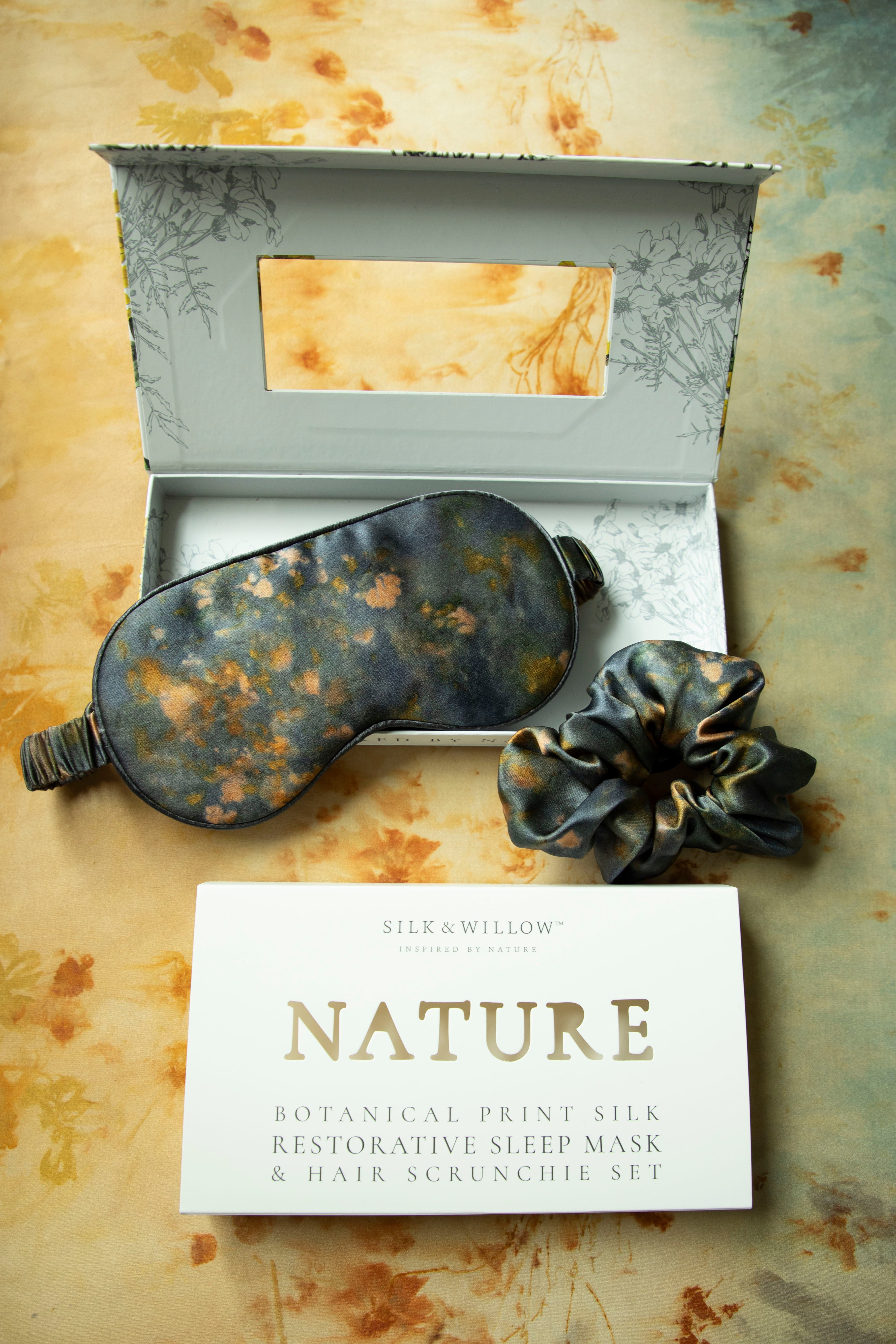 Silk Willows botanical print silk restorative sleep mask and hair scrunchie set on a textured surface.